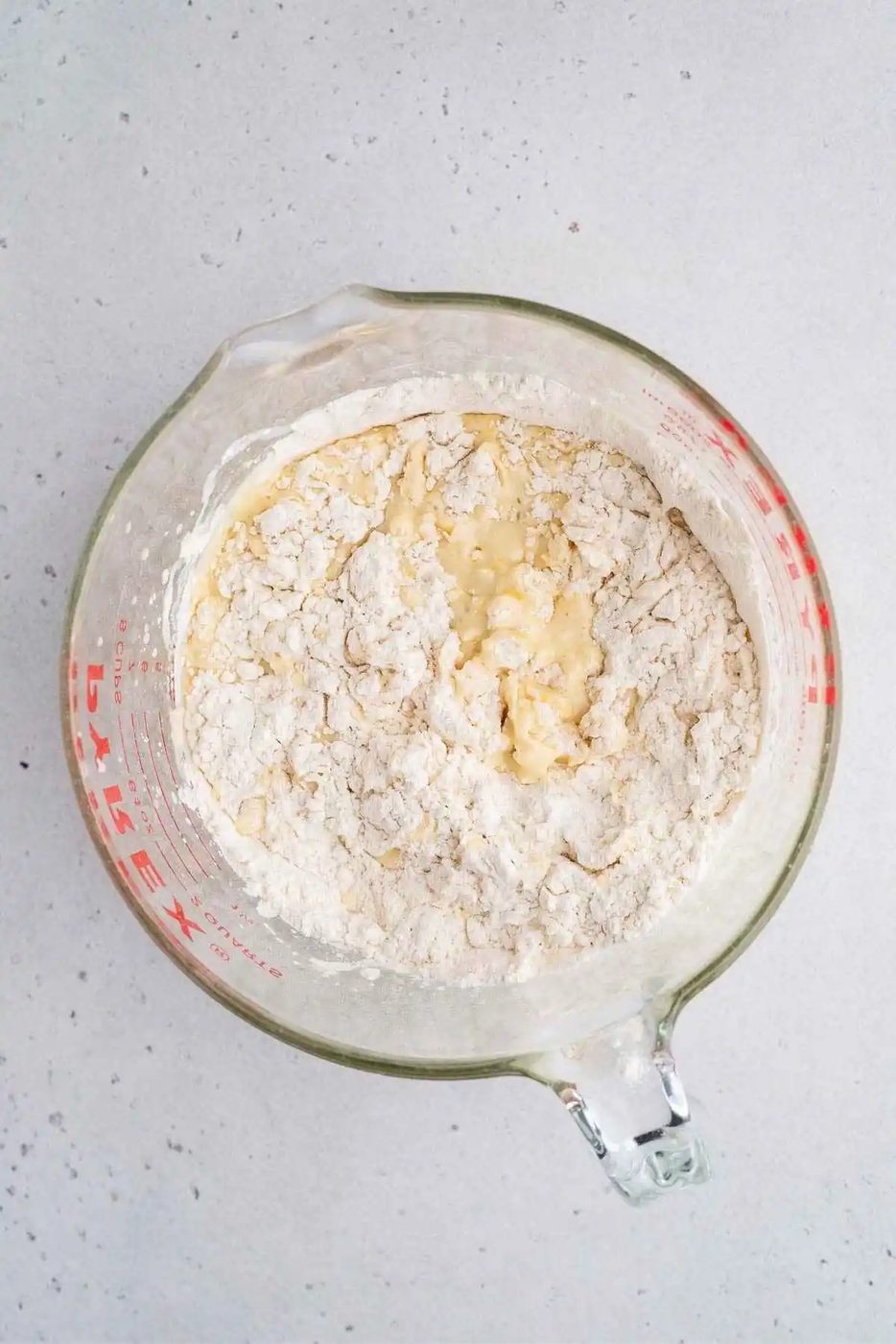 Lemon poppy seed muffin batter in a large glass measuring bowl with dry ingredients partially mixed in.