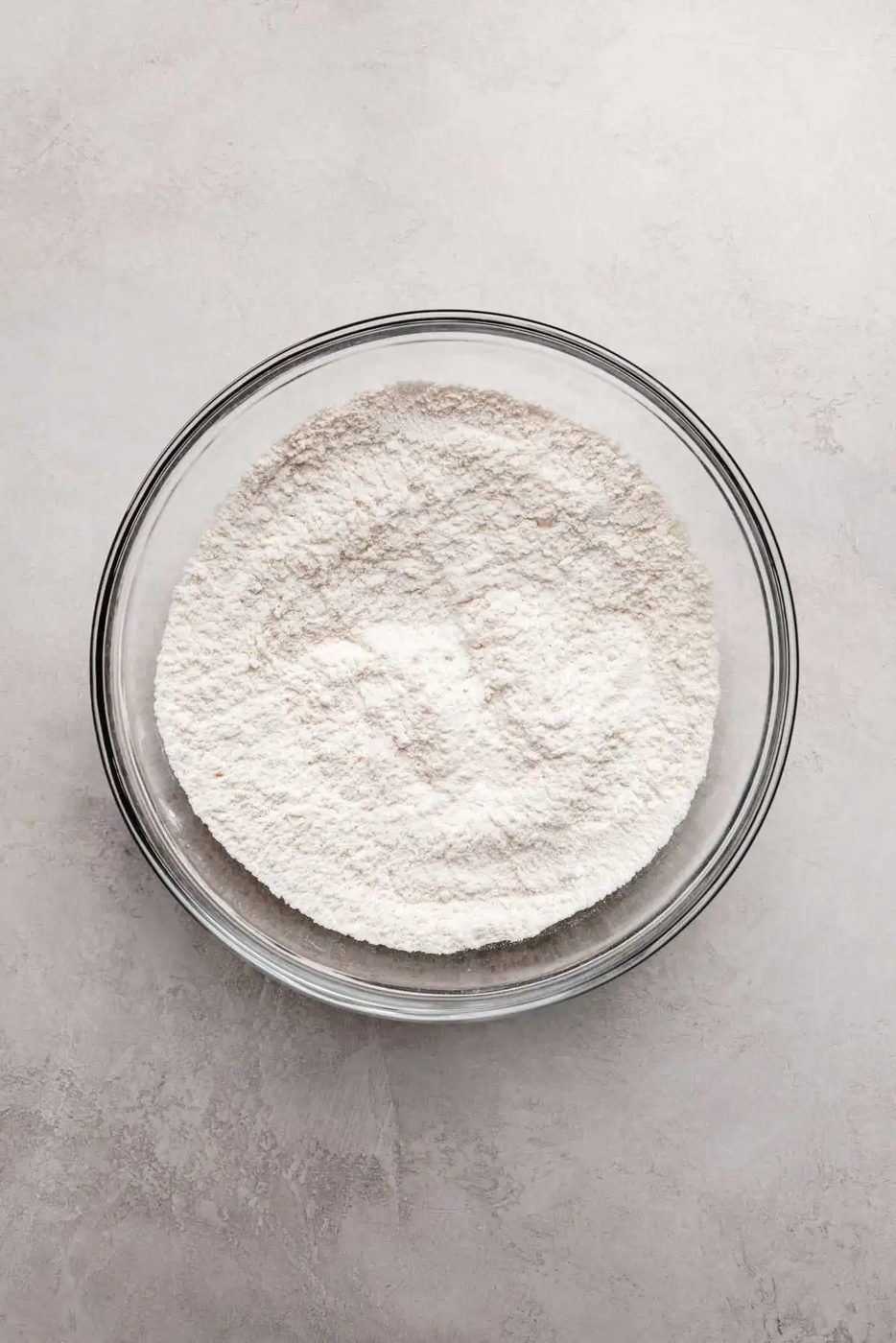Whisked all purpose flour, baking powder, and salt in a large glass mixing bowl on a grey marbled background.