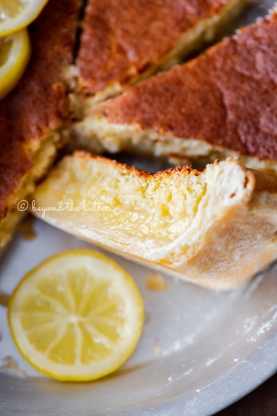 Close up of lemon sponge pie with one slice on its side paired with a slice of lemon below it | All Images © Sovuh