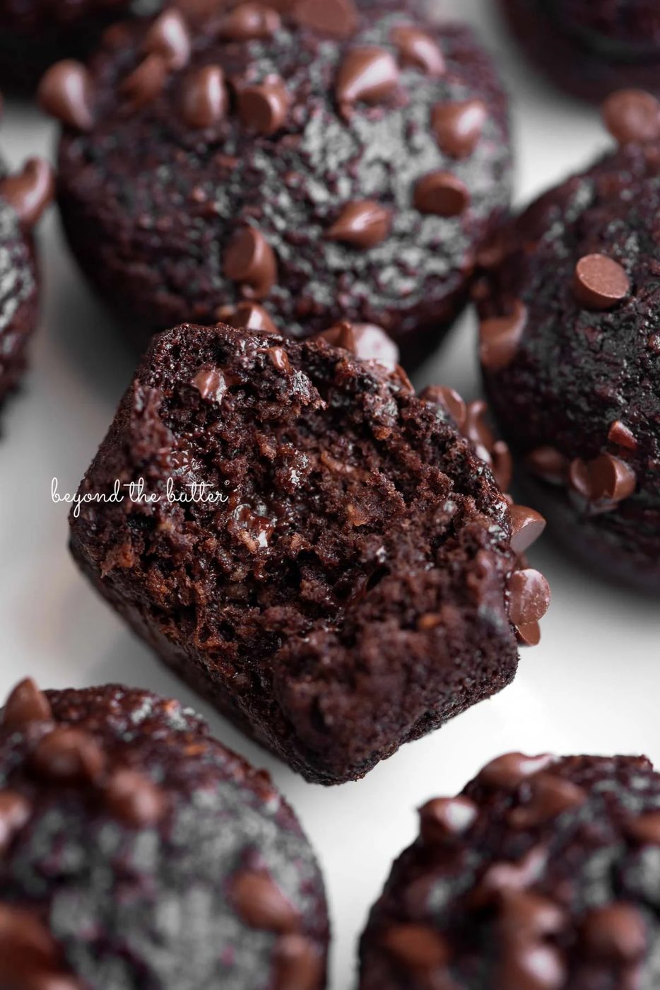 Mini chocolate banana oatmeal muffins topped with mini chocolate chips placed close together with a bit taken out of the center muffin on a white background.