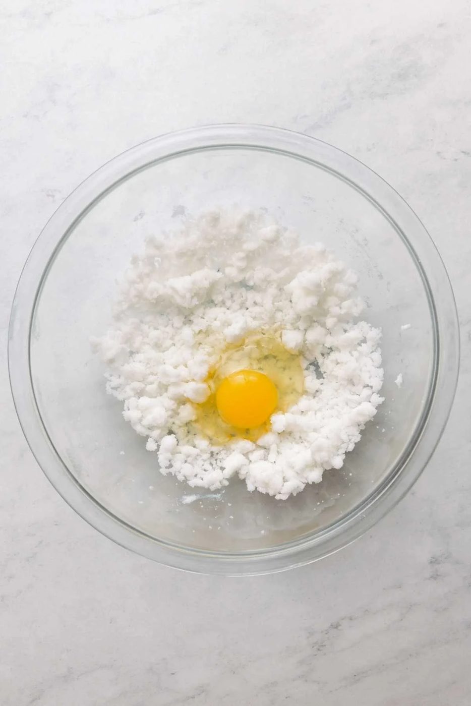Vegetable shortening and granulated sugar beaten together in a large glass mixing bowl with an egg cracked on top.