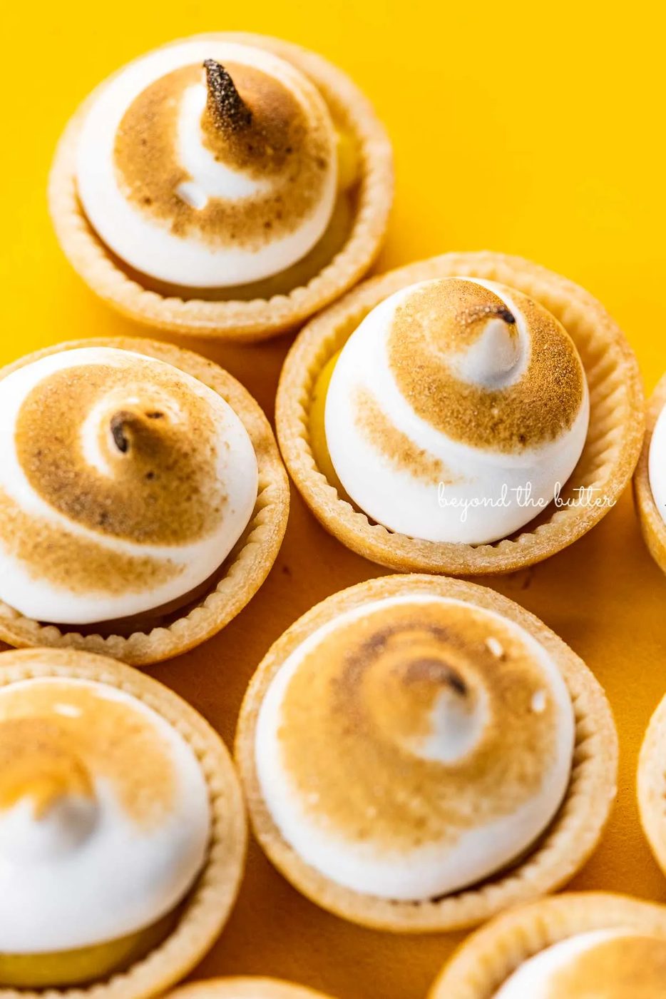 Angled image of mini lemon meringue pies on a yellow background | © Sovuh