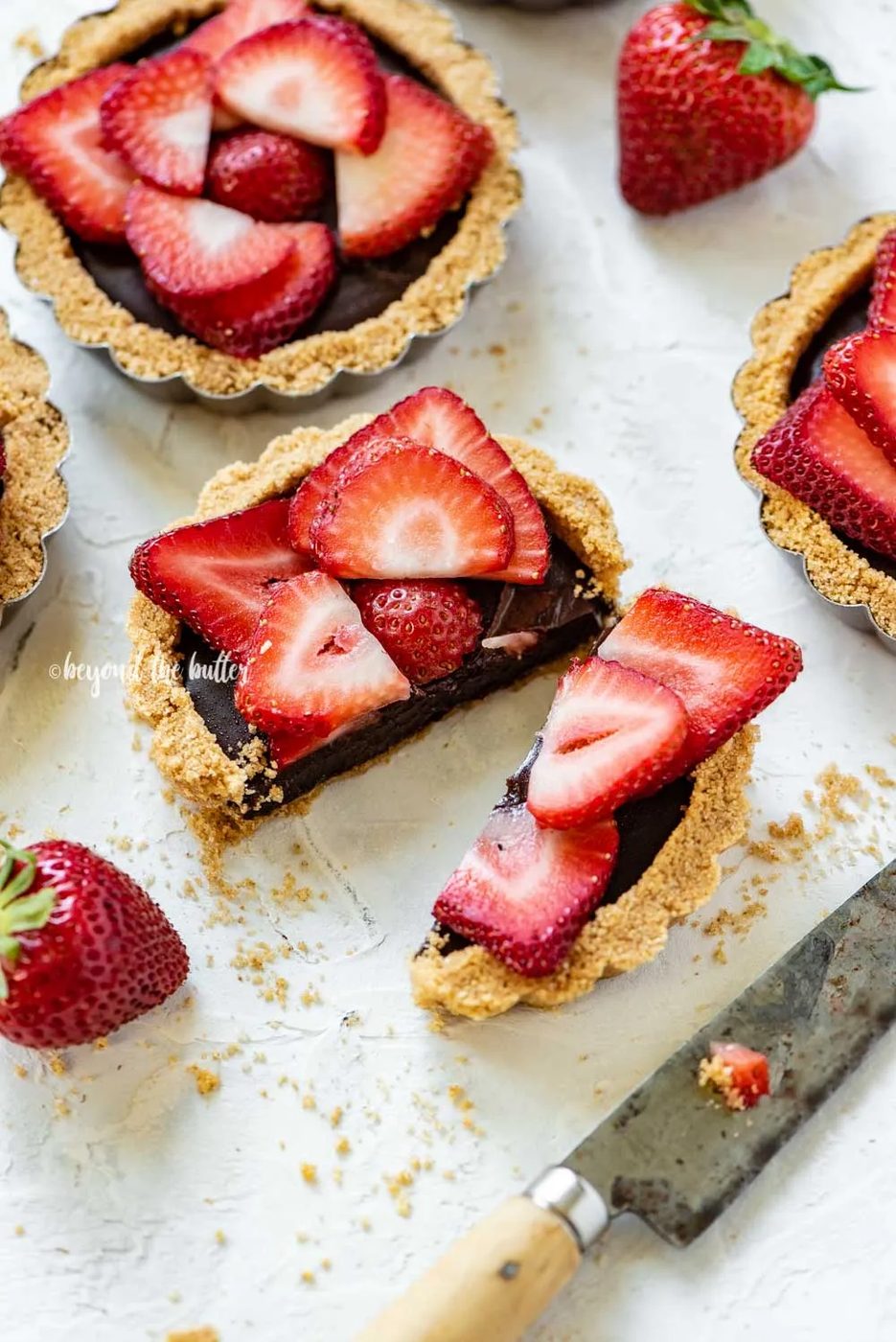Angled image of mini strawberry nutella tarts on white stucco background with one sliced in half and opened | All Images © Sovuh