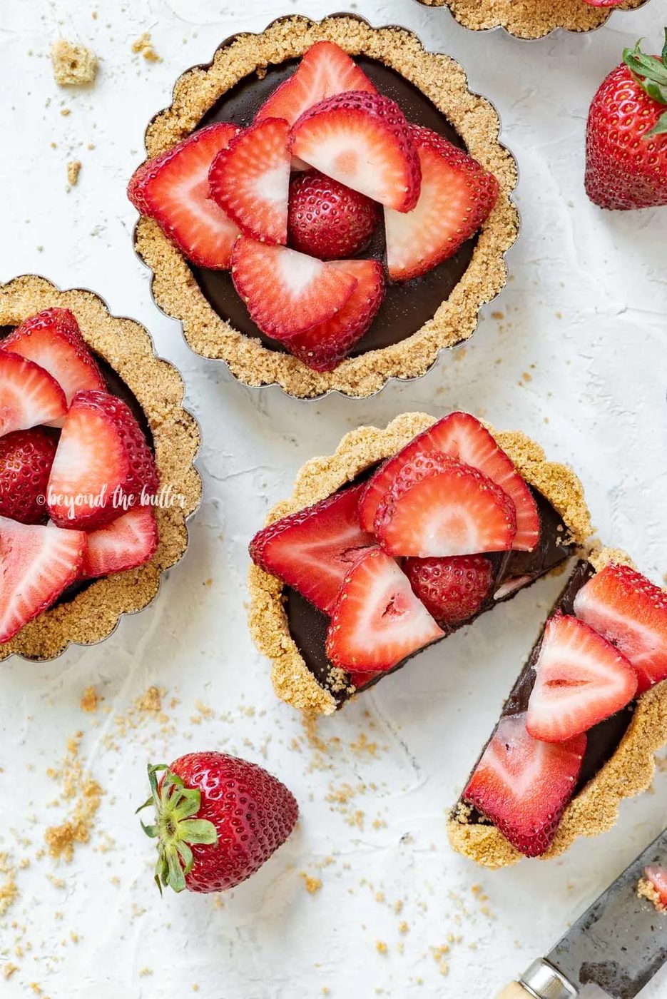Overhead image of mini strawberry nutella tarts on white stucco background with one sliced in half and opened | All Images © Sovuh