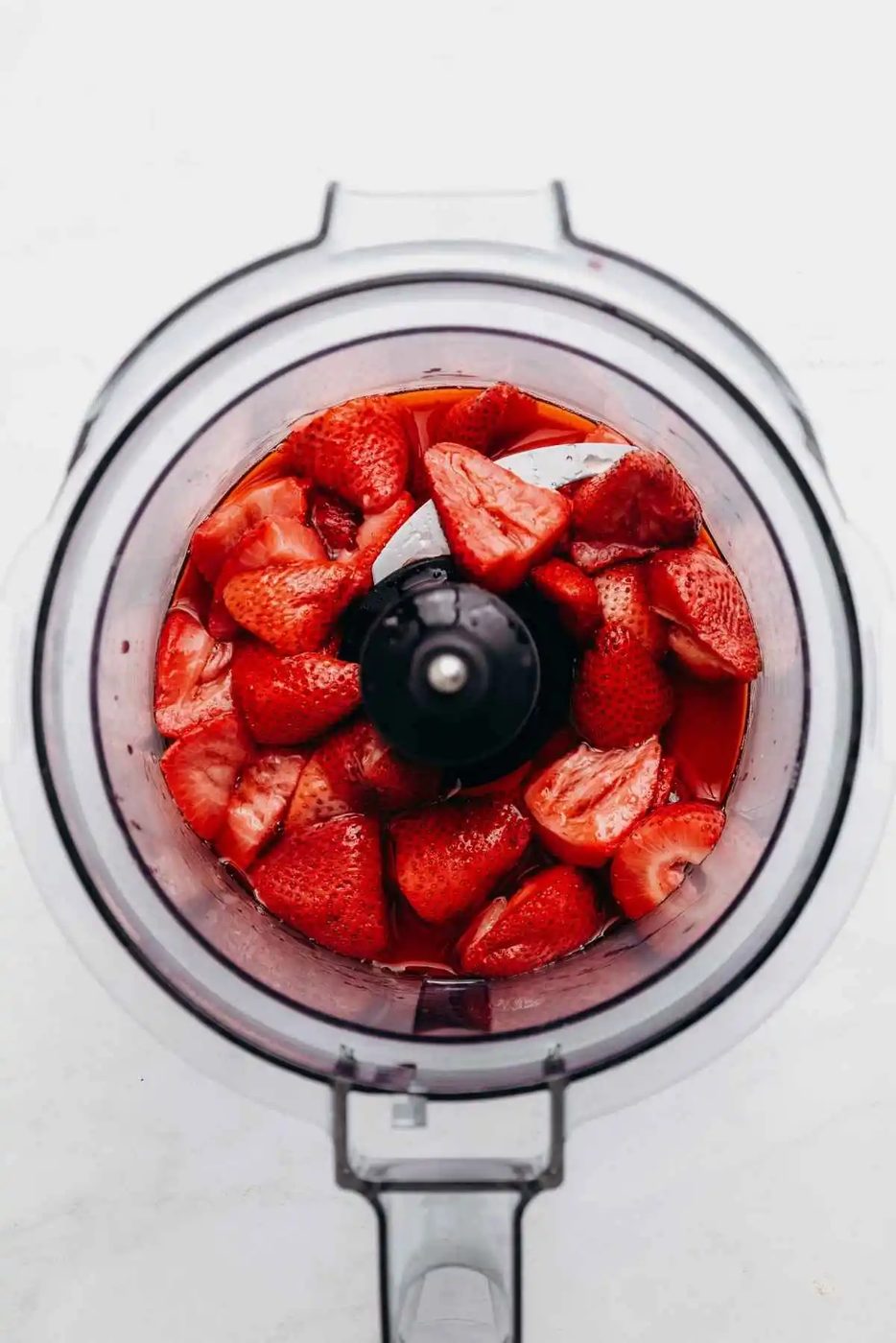 Roasted strawberries in a food processor on a white and grey textured background.