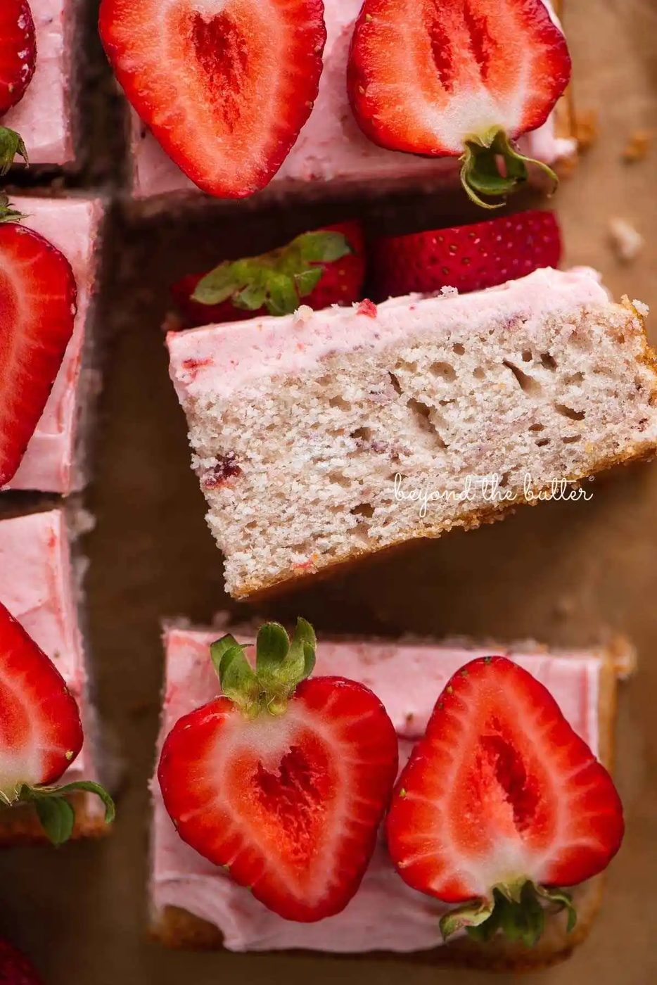 Slices of mini strawberry sheet cake topped with strawberry buttercream frosting and fresh strawberries with one slice on its side.