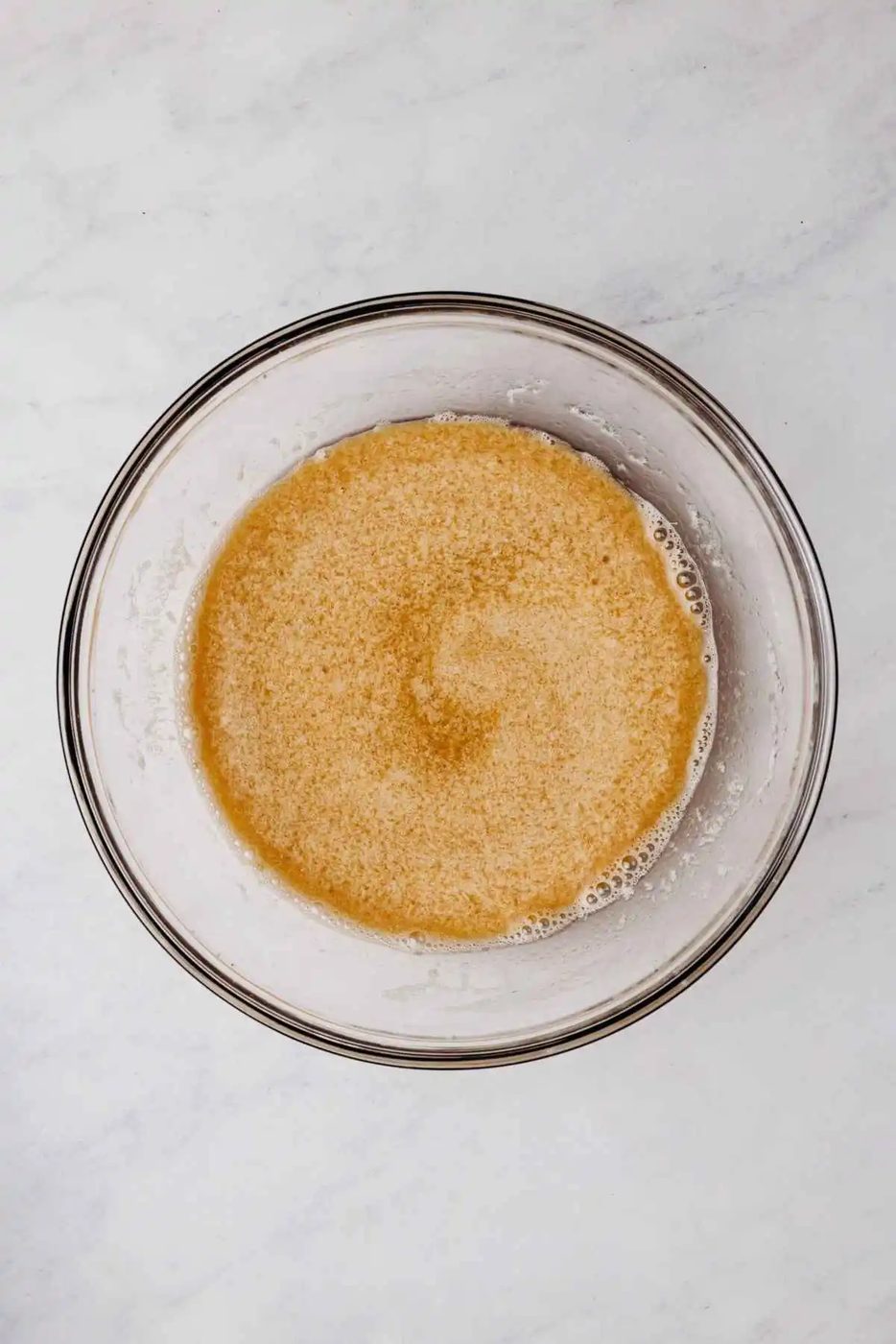 Espresso powder mixture added to chocolate cupcake wet ingredients in a medium size glass mixing bowl on a grey marbled background.