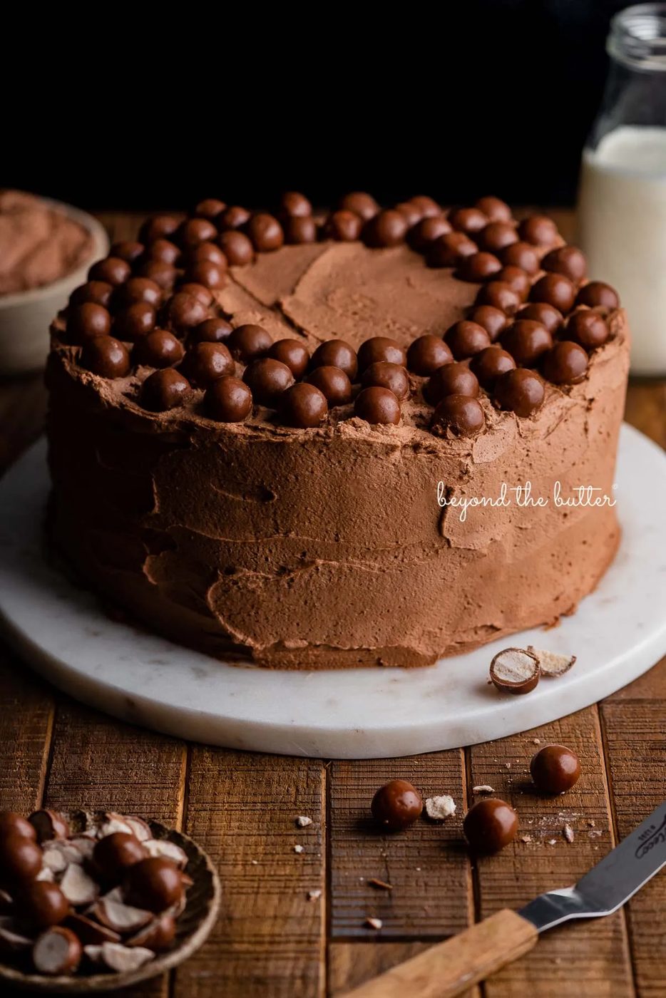 Malted chocolate whipped cream frosted banana cake on a marble cake stand and dark wood background | © Sovuh