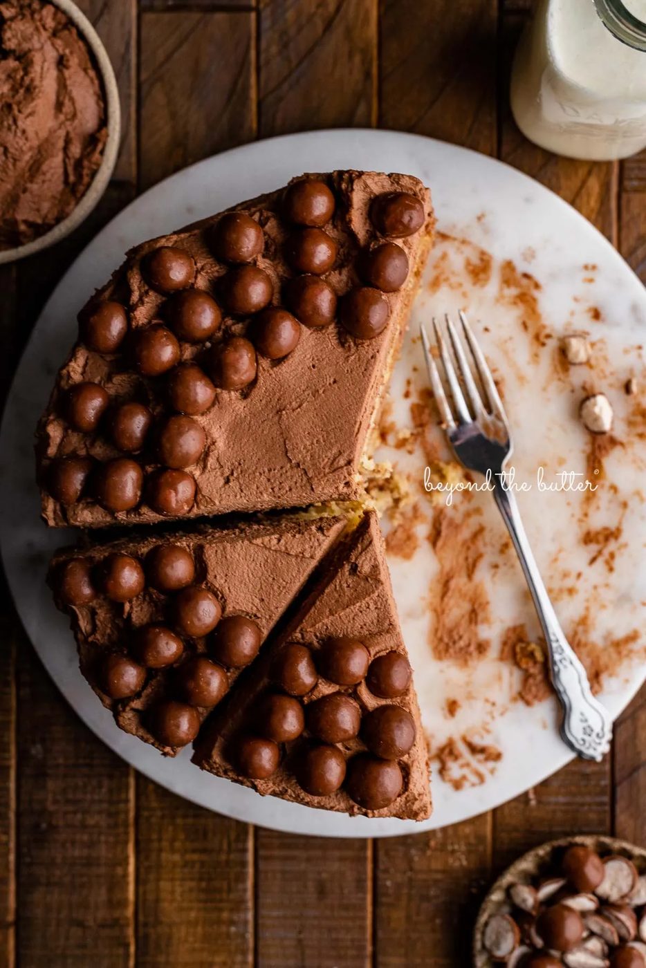 Top down view of 2 layer tender banana cake frosted with malted chocolate mascarpone whipped cream and garnished with malted chocolate balls on marble cake board | © Sovuh