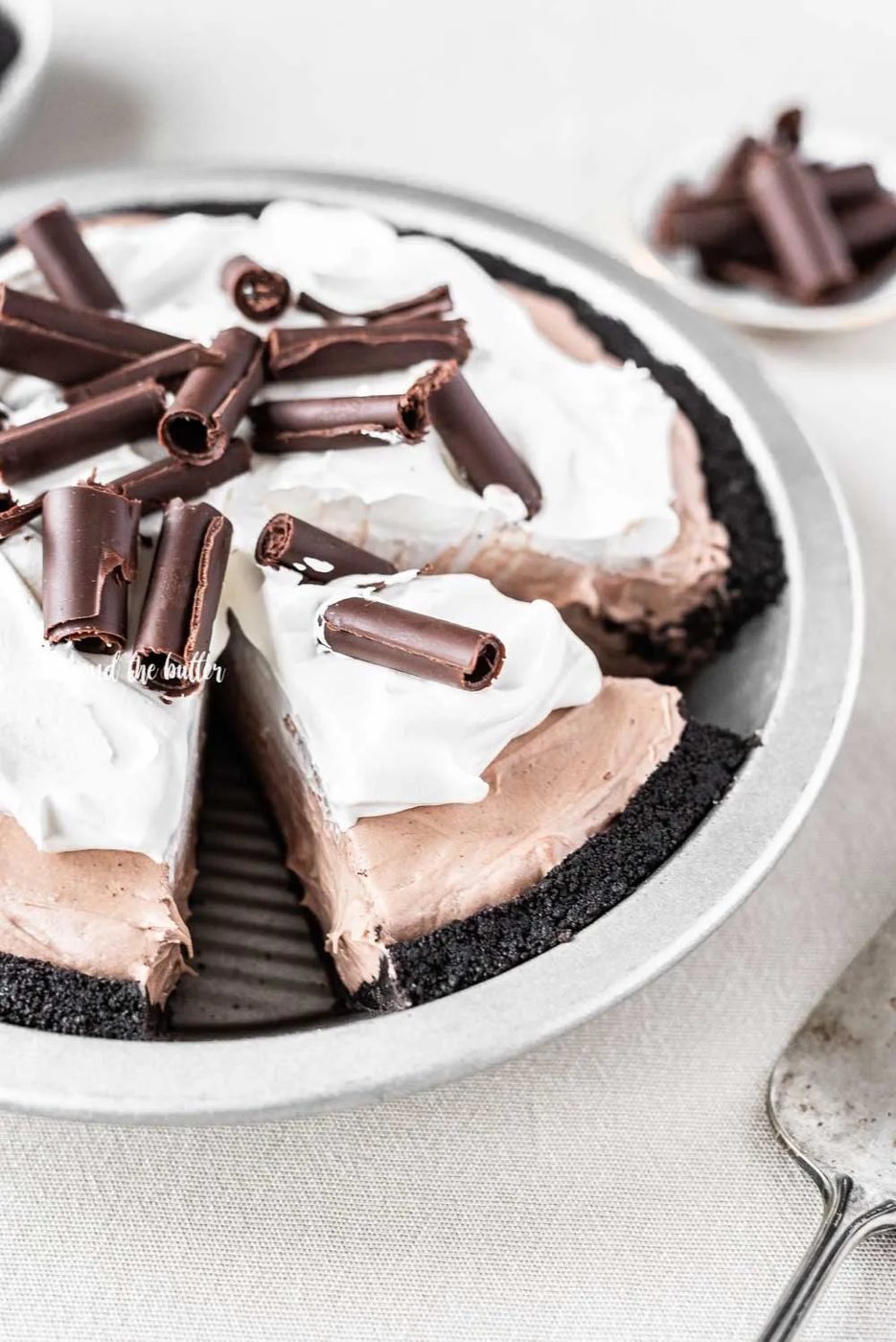 Angled image of sliced no-bake chocolate cream pie with chocolate wafer crust and garnished with Cool Whip and chocolate curls | All Images © Sovuh