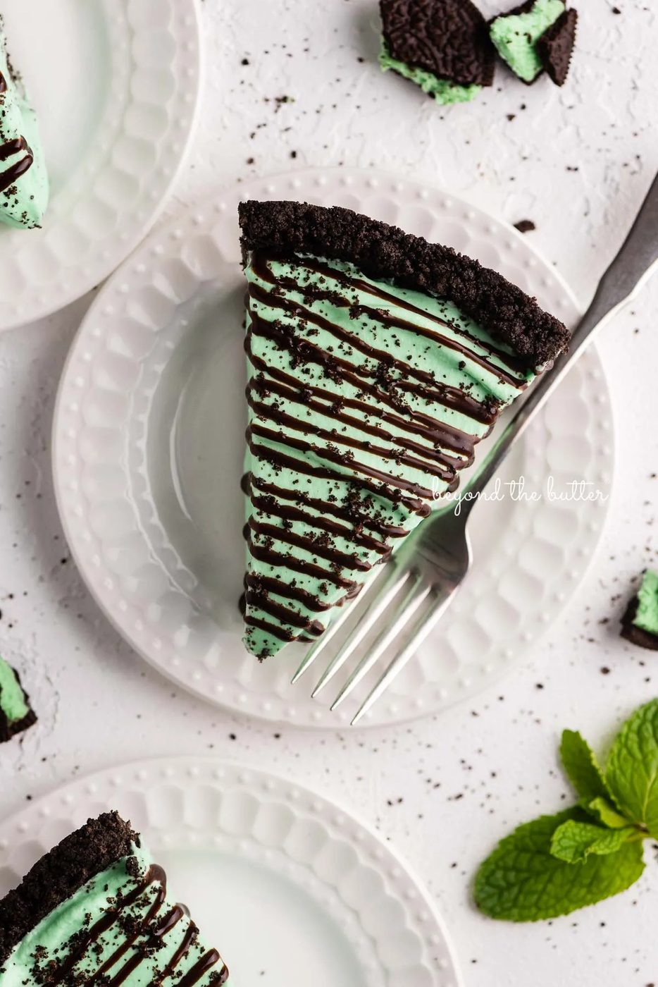 Dessert plates with slices of no bake mint chocolate pie with chocolate syrup drizzled over the top | © Sovuh