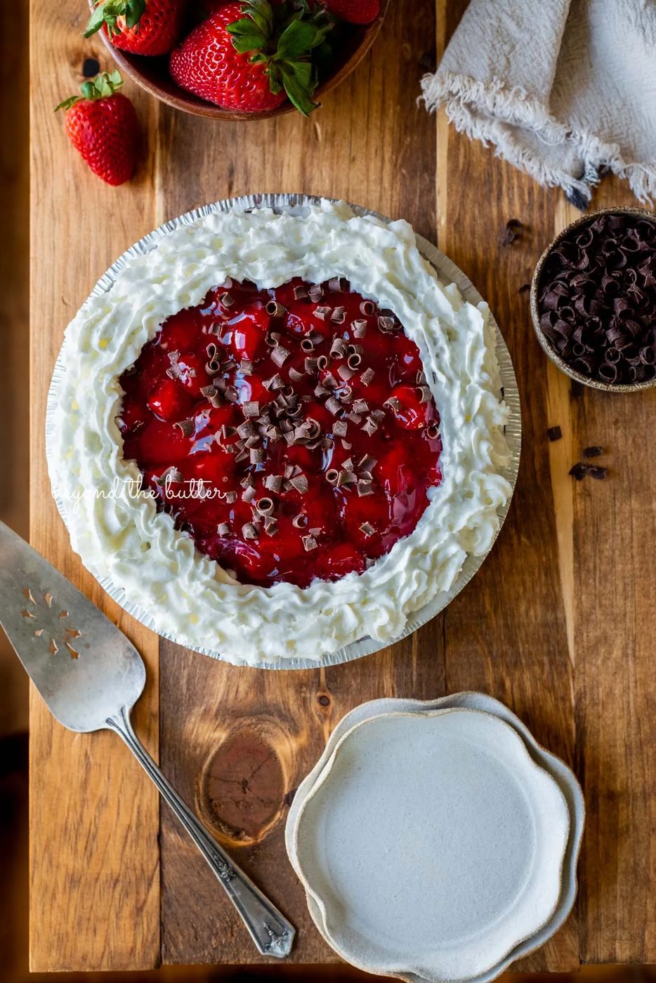 Decorated no bake strawberry chocolate pie with small bowl of chocolate curls and strawberries, dessert plates, and pie server on wood table | All images © Sovuh