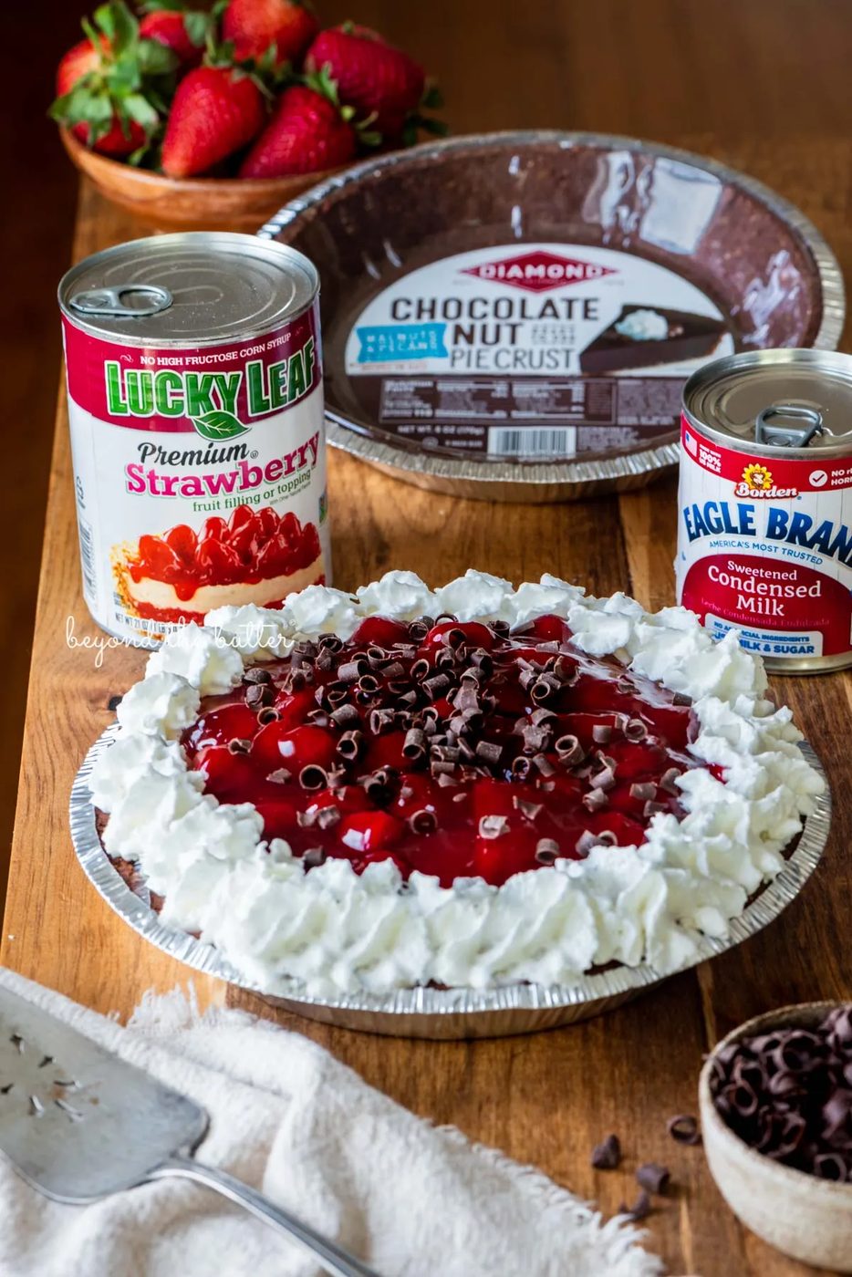Diamond of CA chocolate nut pie crust, Lucky Leaf strawberry pie filling, and Eagle Brand sweetened condensed milk with decorated no bake strawberry chocolate pie with small bowl of chocolate curls and strawberries on wood table | All images © Sovuh