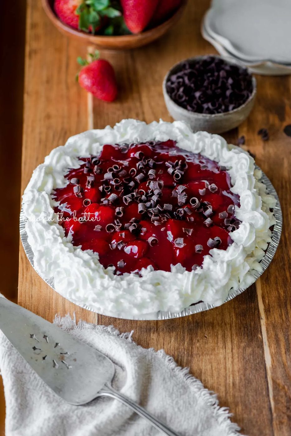 Decorated no bake strawberry chocolate pie with small bowl of chocolate curls and strawberries, dessert plates, and pie server on wood table | All images © Sovuh