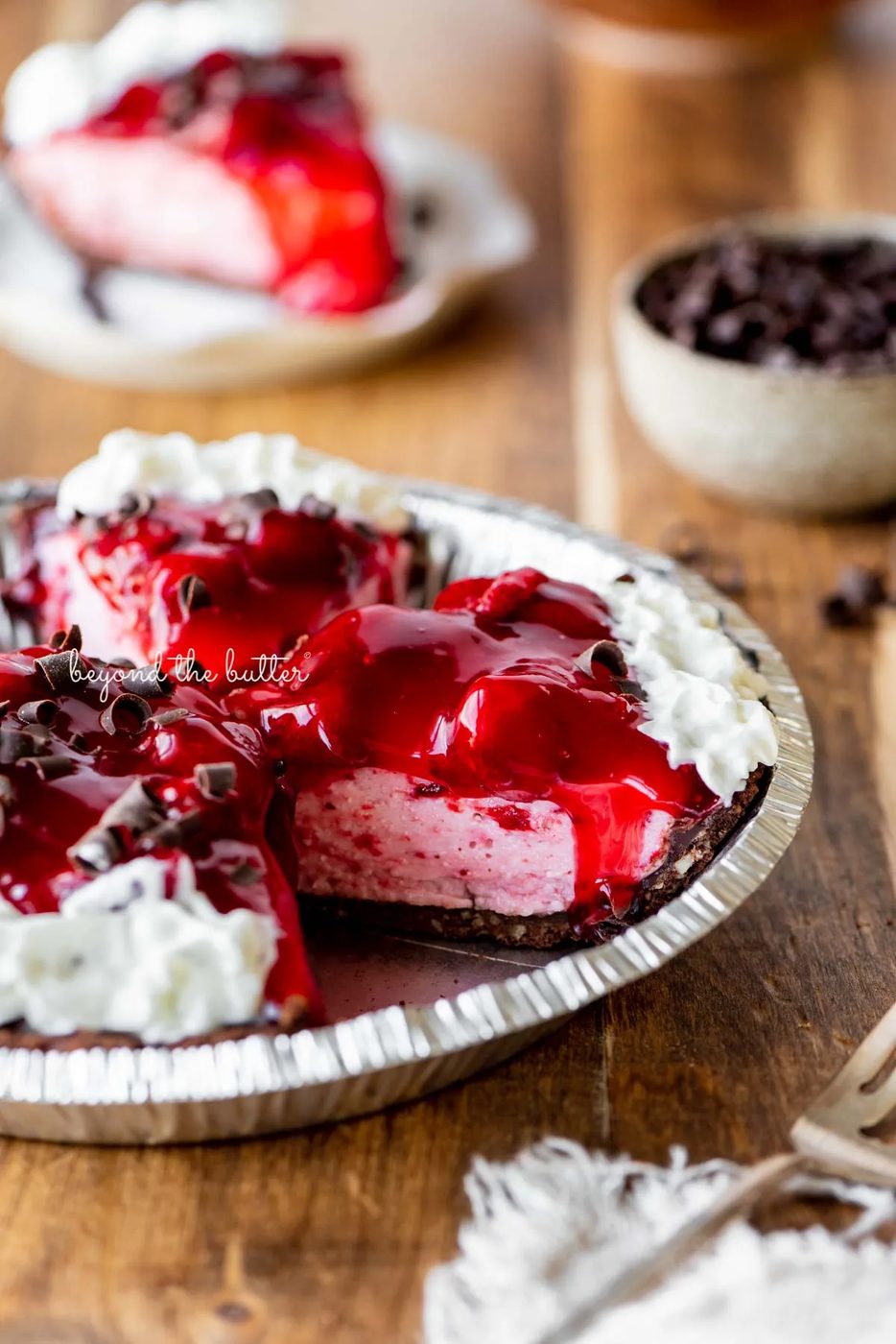 Sliced no bake strawberry chocolate cream pie on wood table with a fork and small bowl of chocolate curls nearby | All images © Sovuh