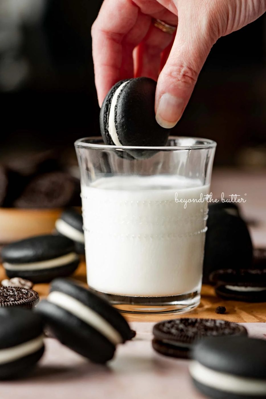 Hand dipping an oreo macaron in a glass of milk with more oreo macarons and oreo cookies around it | © Sovuh