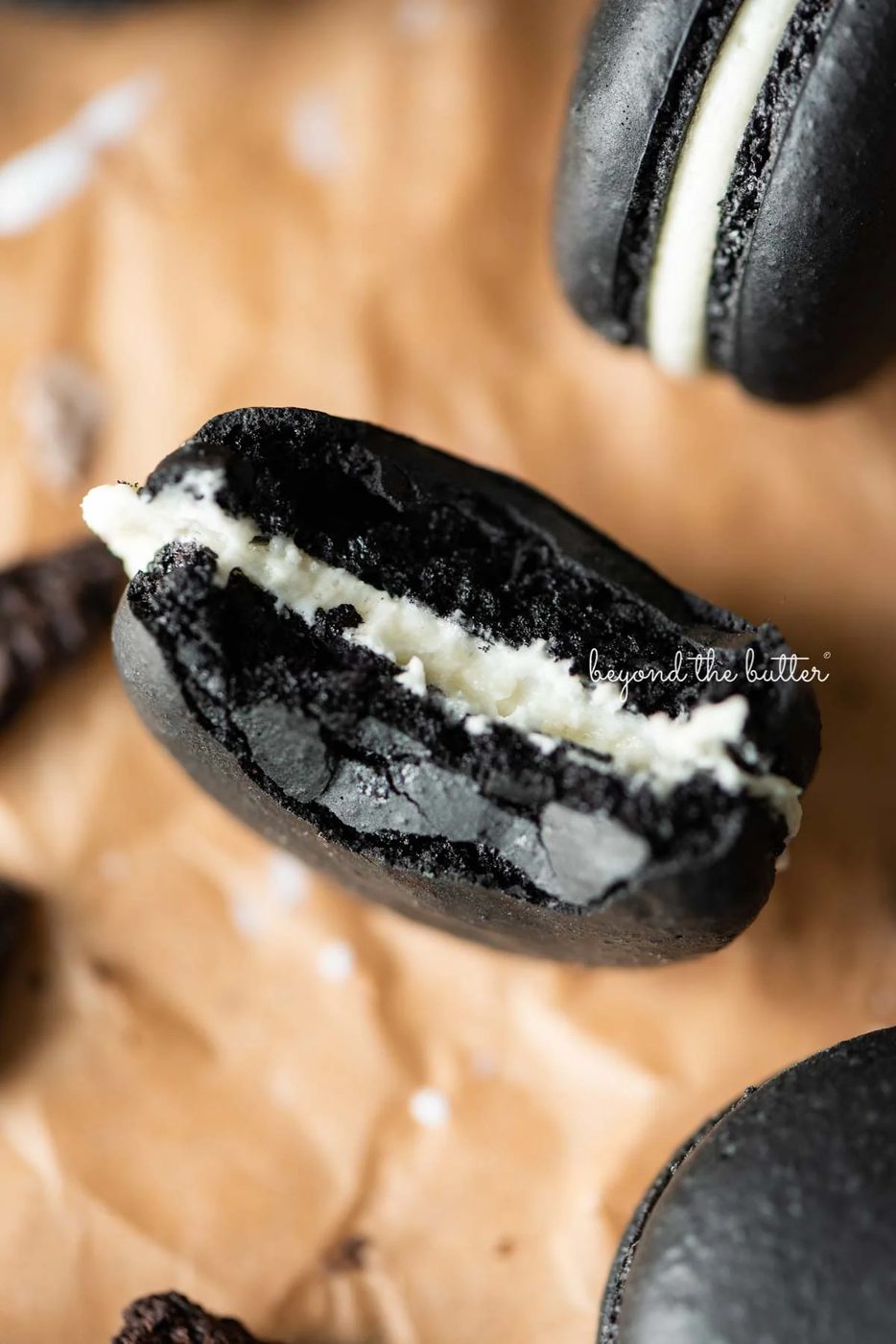 Half eaten oreo macaron on parchment paper surrounded by oreo macarons and broken pieces of oreo cookies | © Sovuh