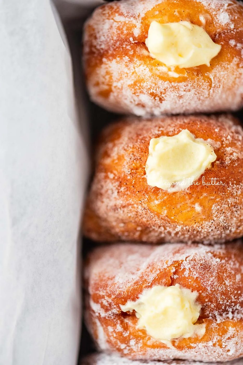 Close up of house-made pennsylvania dutch fasnacht doughnuts filled with vanilla pastry cream wrapped in parchment paper in a loaf pan | © Sovuh