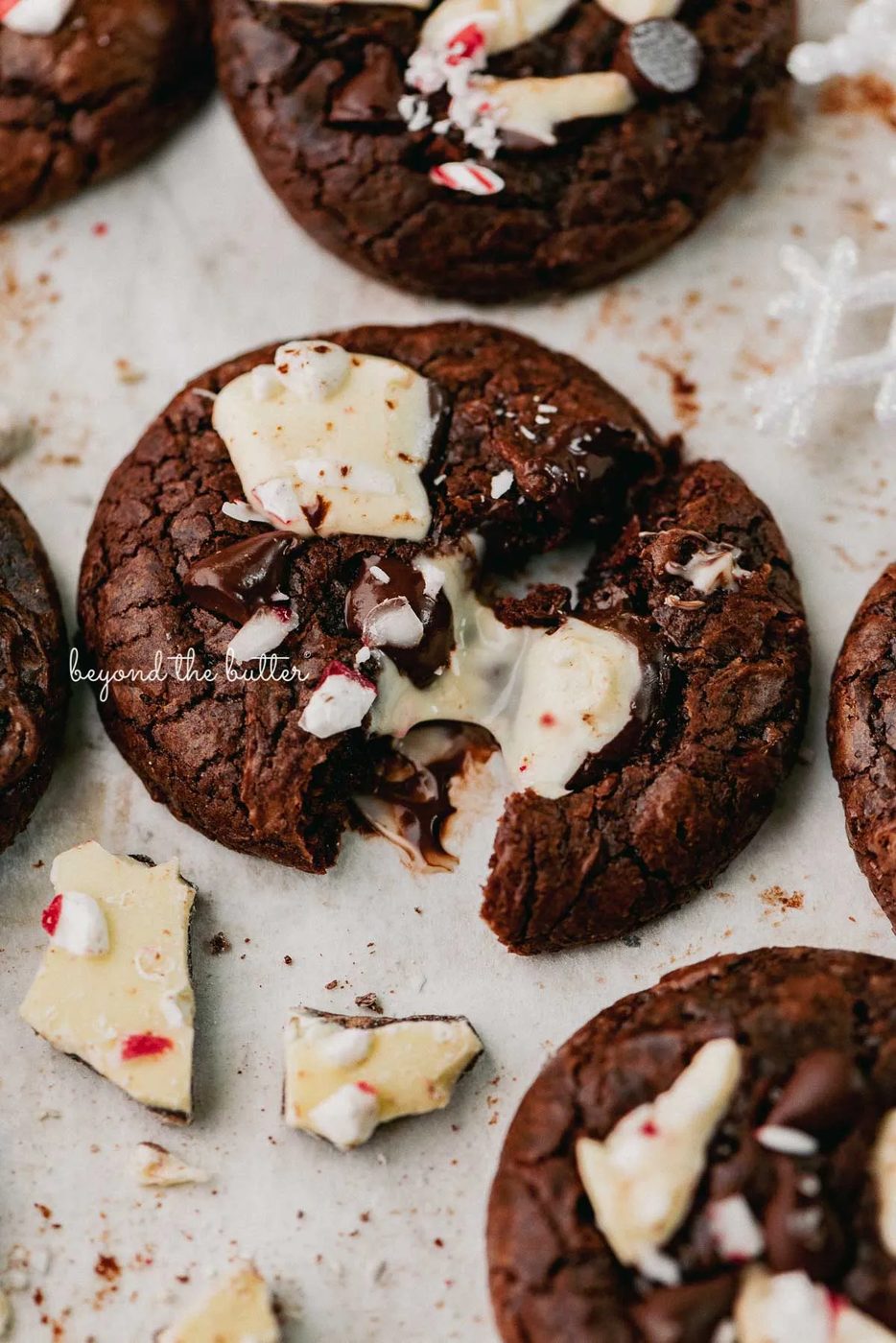 A split peppermint bark brownie crinkle cookie on a parchment paper lined baking sheet | © Beyond the Buter