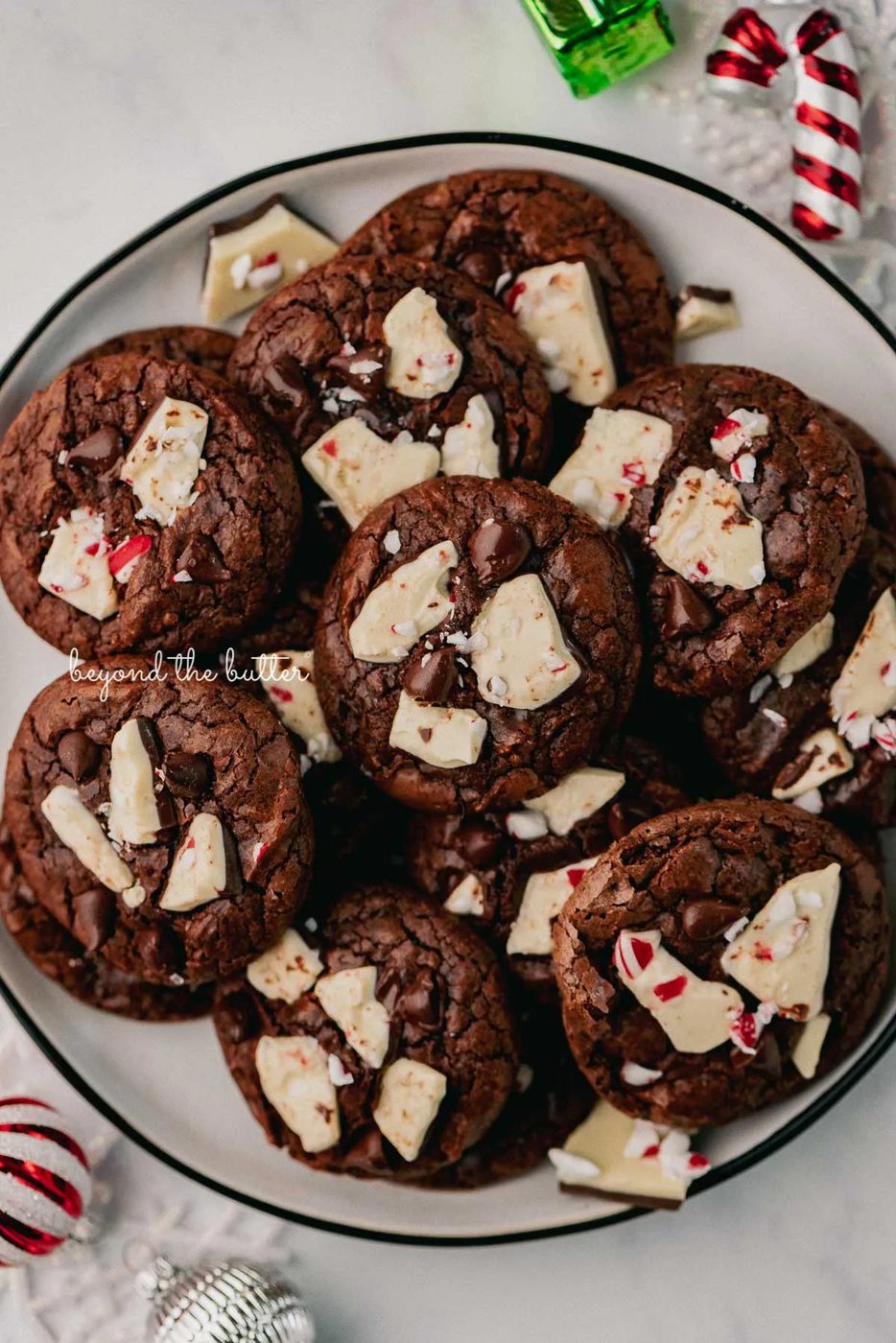 Plate full of peppermint bark brownie crinkle cookies with ornaments around the plate | © Sovuh