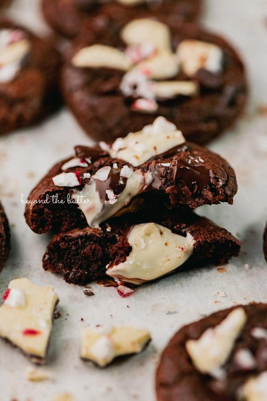 A split peppermint bark brownie crinkle cookie on a parchment paper lined baking sheet | © Beyond the Buter