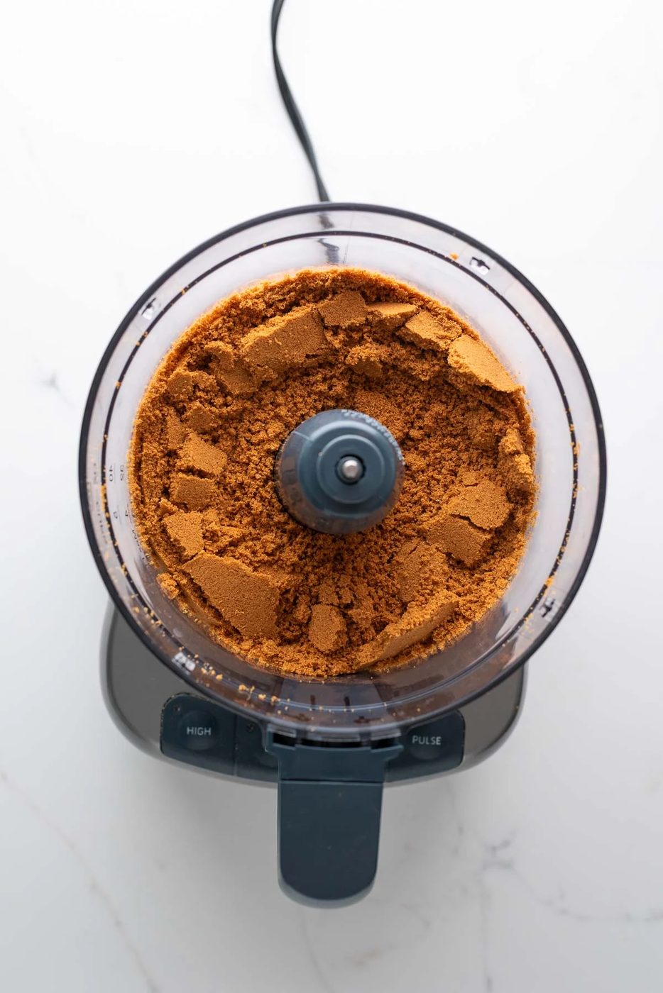 Fine speculoos cookie crumbs processed in a food processor on a white marbled background.