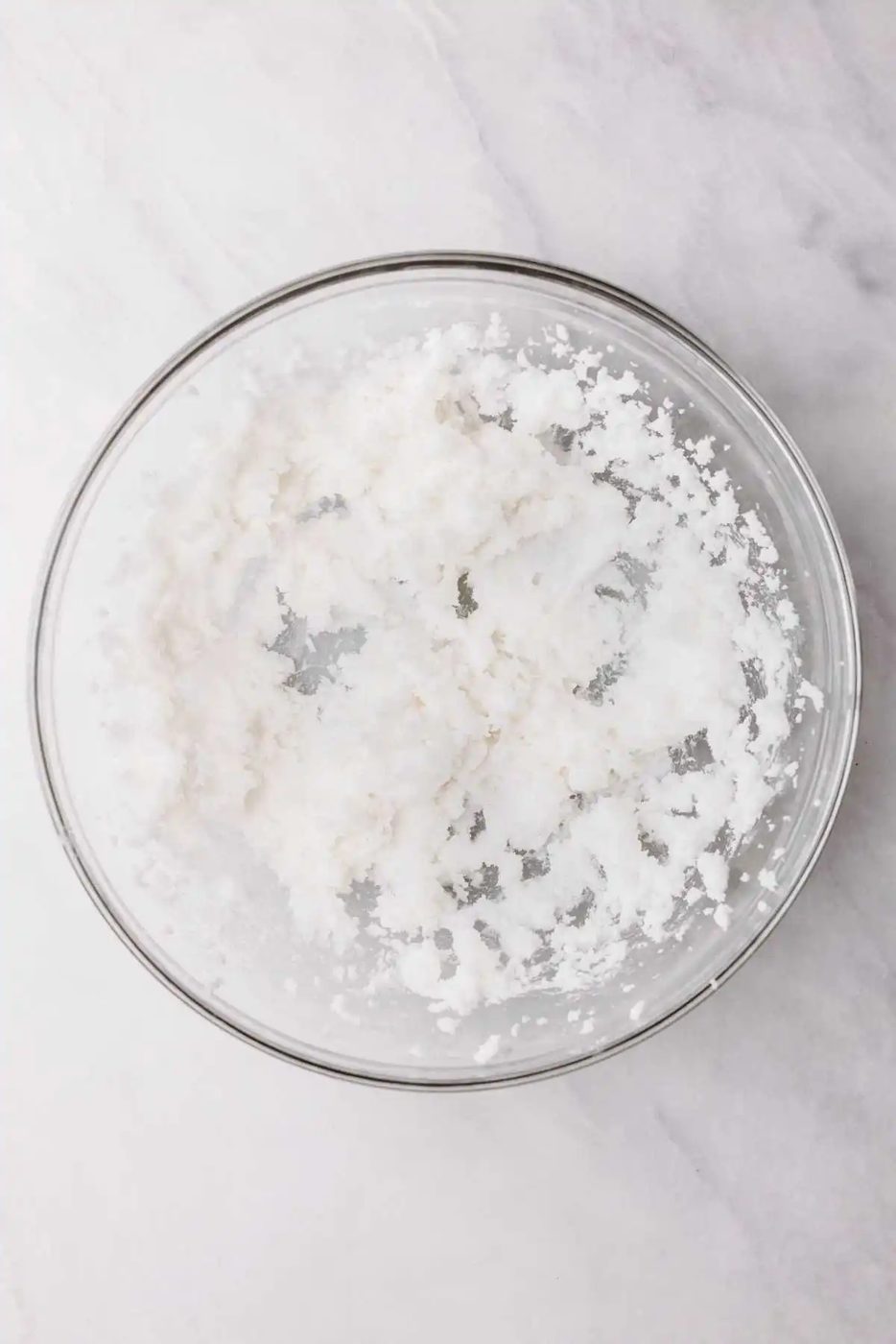 Vegetable shortening and granulated sugar beaten together in a large glass mixing bowl on a light grey textured background.