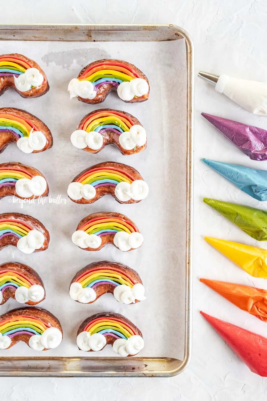 Overhead image of just decorated rainbow donuts on a baking sheet with piping bags filled with buttercream | All Images © Sovuh, LLC