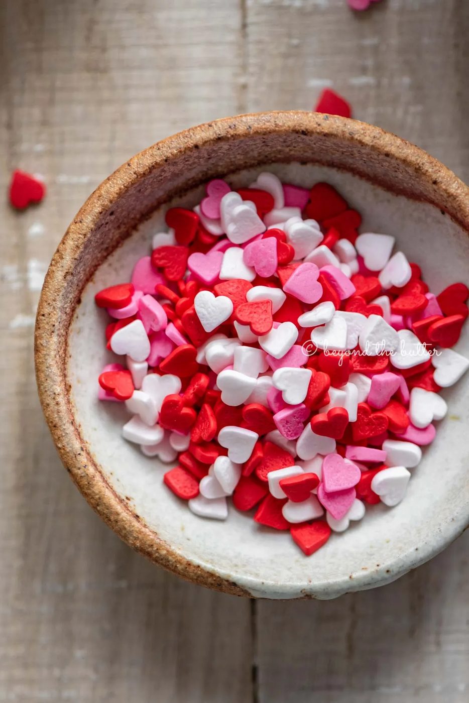Small bowl of Valentine's Day heart sprinkles House-made red velvet cupcakes with one opened and half eaten with a small bowl of Valentine's Day sprinkles on light wood background | All images © Sovuh