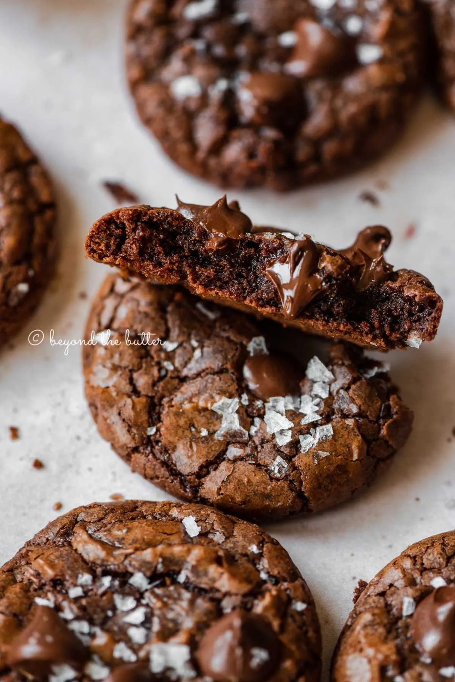Salted brownie cookie split in half showing with melted chocolate chips peaking through | All Images © Sovuh