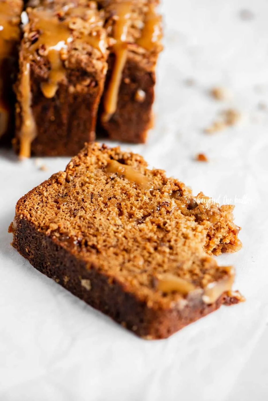 Angled image of slices of salted caramel banana nut bread on parchment paper with a bread knife next to it | All Images © Sovuh