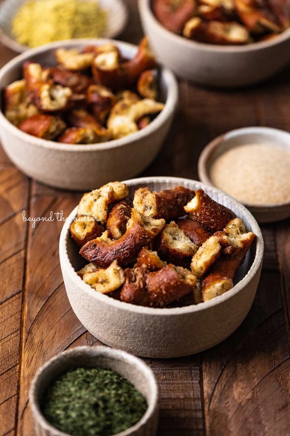Small snacking bowls filled with seasoned pretzels with dill weed and garlic powder in side bowl on dark wood background from Sovuh.com | © Sovuh