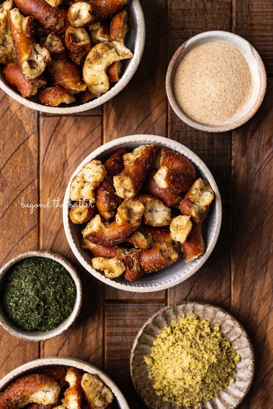 Small ceramic snacking bowls filled with seasoned pretzels with dill weed and garlic powder in side bowl on dark wood background from Sovuh.com | © Sovuh