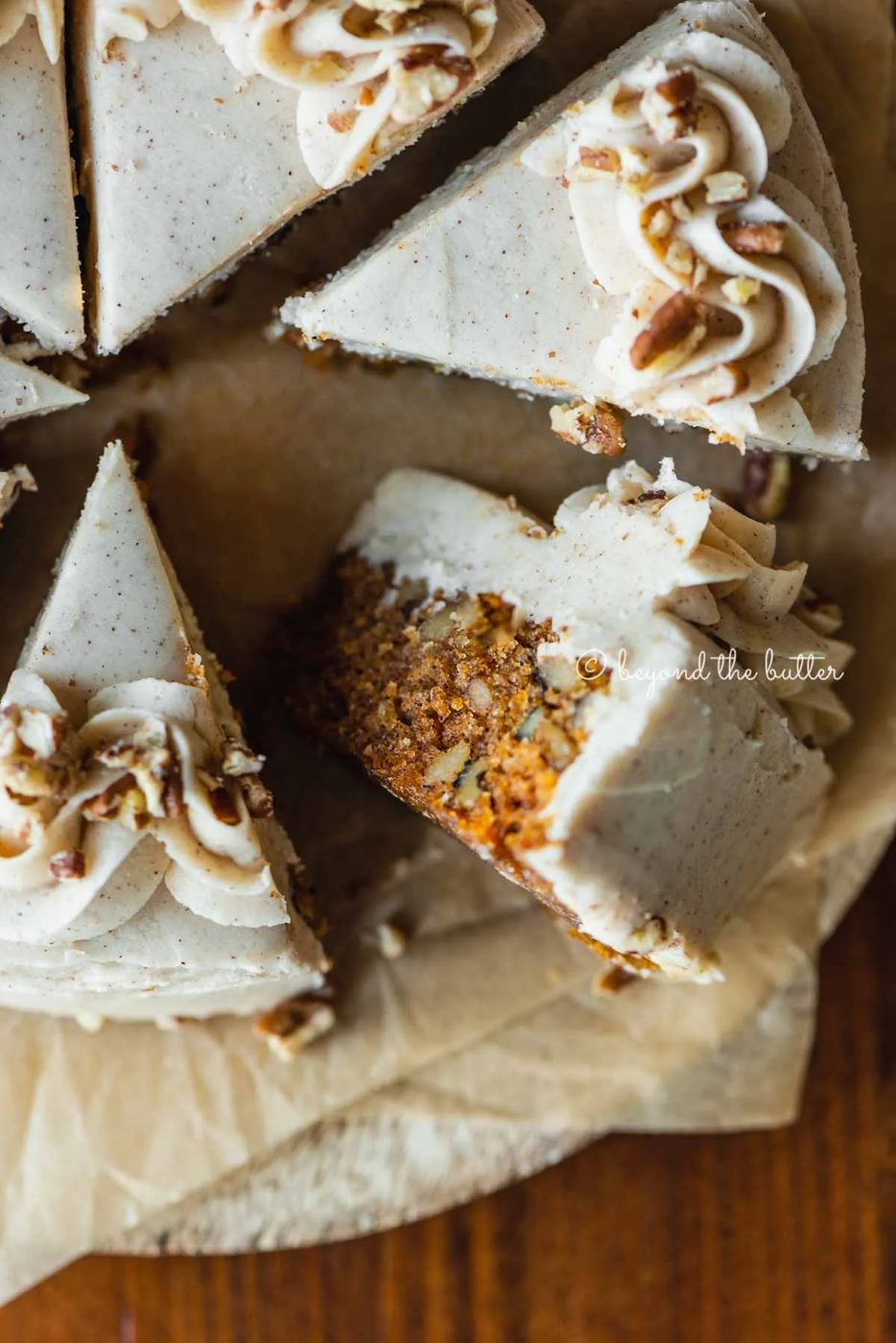 Overhead closeup image of single layer carrot cake frosted on parchment paper and placed on a wood dining room table | All Images © Sovuh