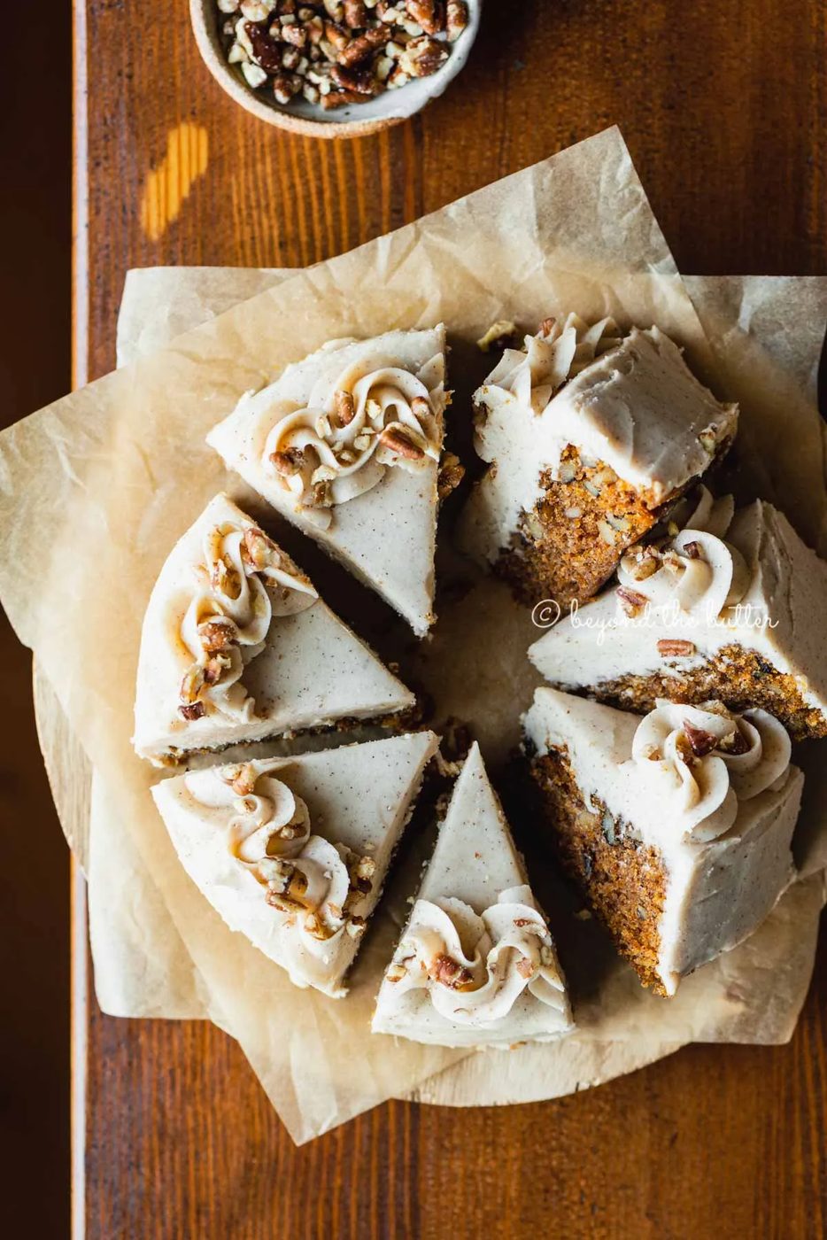 Overhead image of single layer carrot cake frosted on parchment paper and placed on a wood dining room table | All Images © Sovuh