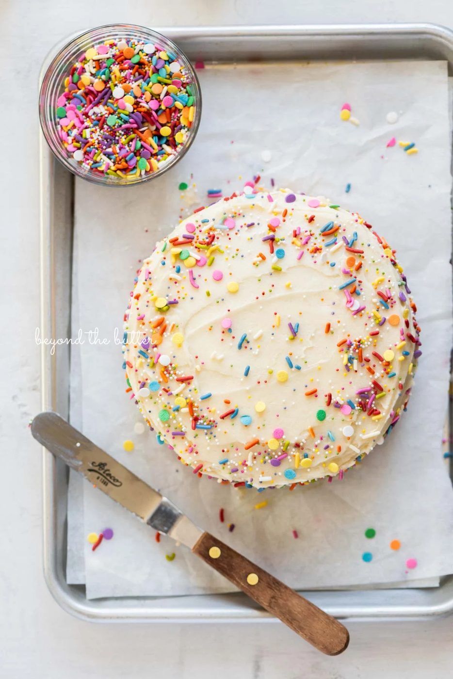 Single layer funfetti cake just frosted and sprinkled on a small parchment paper lined baking sheet from Sovuh.com | All images © Sovuh