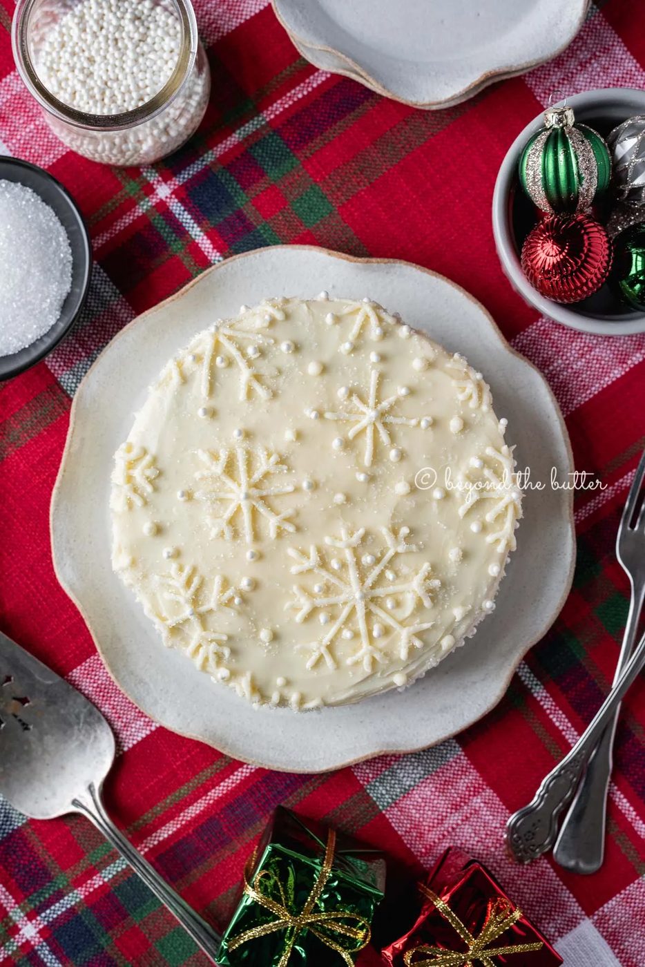 Red velvet cake with cream cheese frosting on a scalloped edge dessert plate with red plaid background | All Images © Sovuh