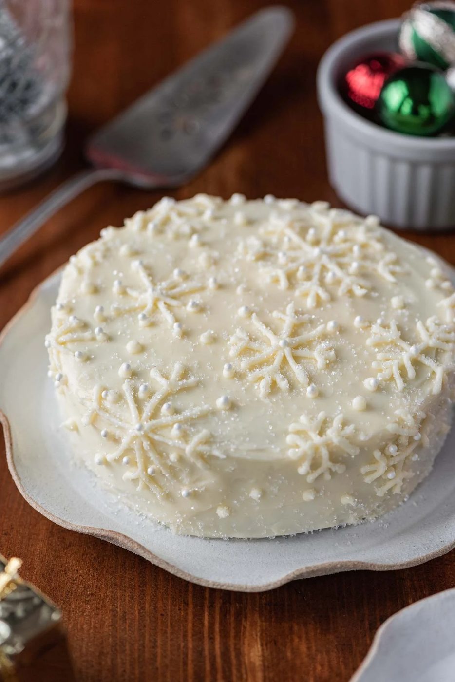 Red velvet cake with cream cheese frosting on a scalloped edge dessert plate with dark wood background | All Images © Sovuh