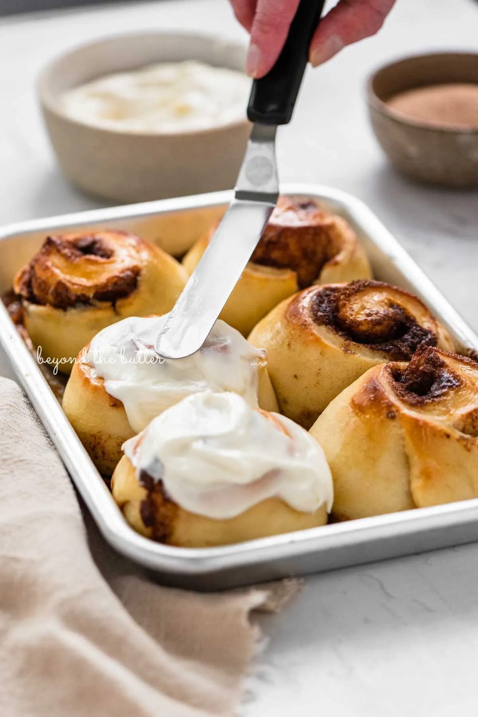 Image of small batch cinnamon rolls being frosted with cream cheese frosting from Sovuh.com | © Sovuh