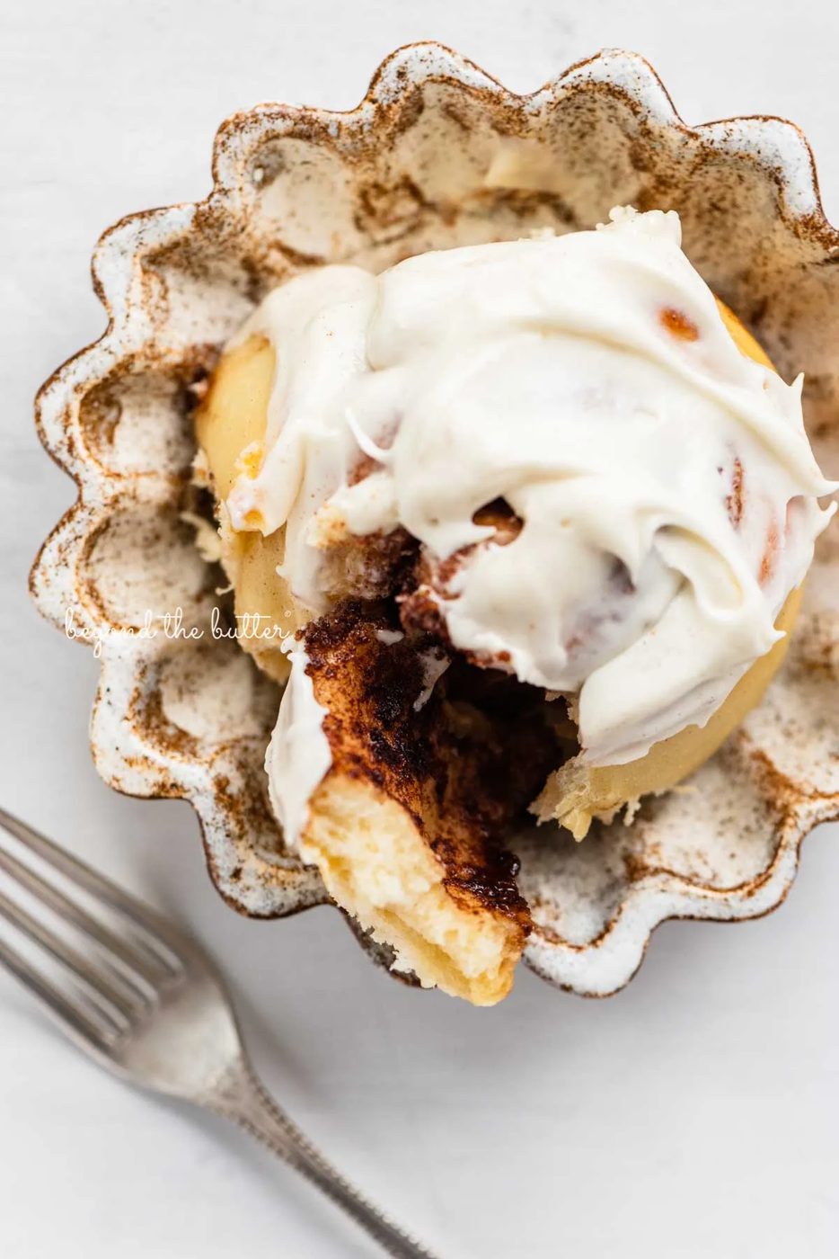 Cream Cheese frosting covered cinnamon roll on small ceramic dessert plate | © Sovuh