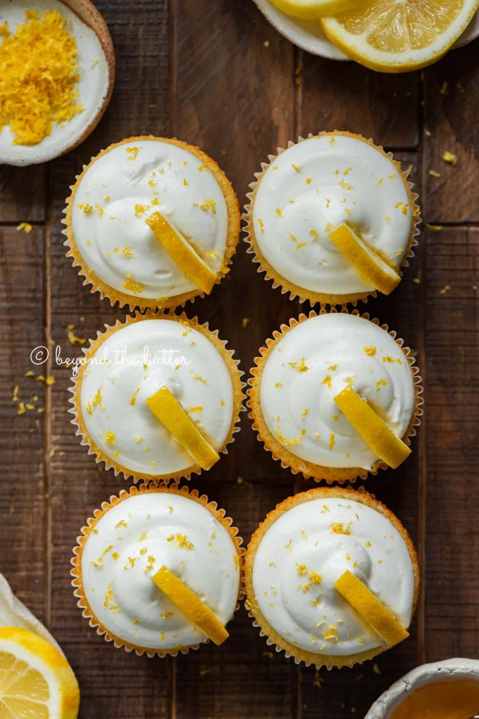 Two rows of small batch lemon cupcakes with lemon cream cheese frosting and garnished with lemon triangles on a dark wood background | All Images © Sovuh