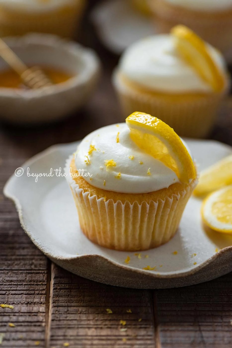 Lemon cupcakes with lemon cream cheese frosting garnished with lemons on small wavy dessert plates | All Images © Sovuh