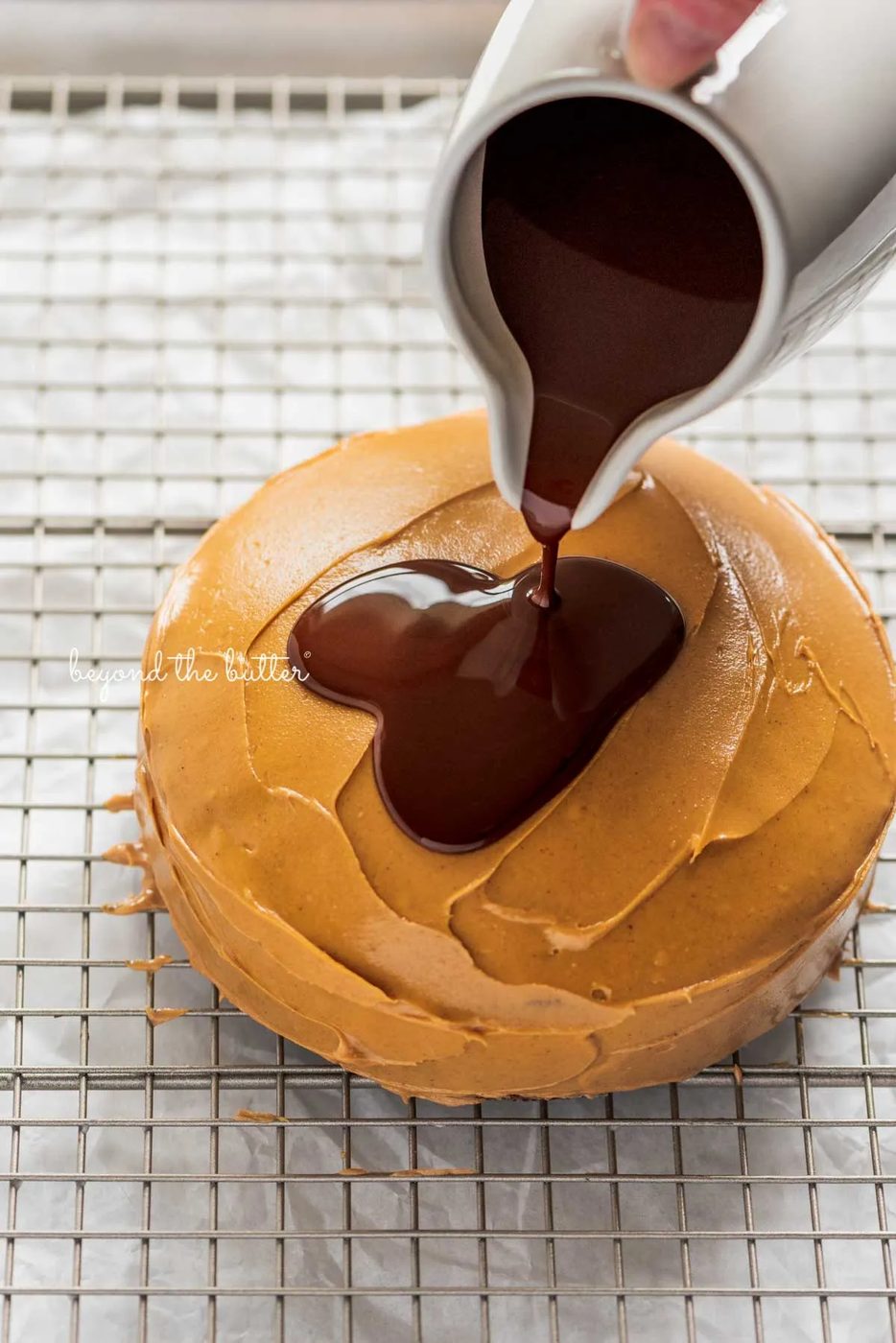 Pouring the melted chocolate over top of the peanut butter layered tandy kake on a wire cooling rack baking sheet | © Sovuh