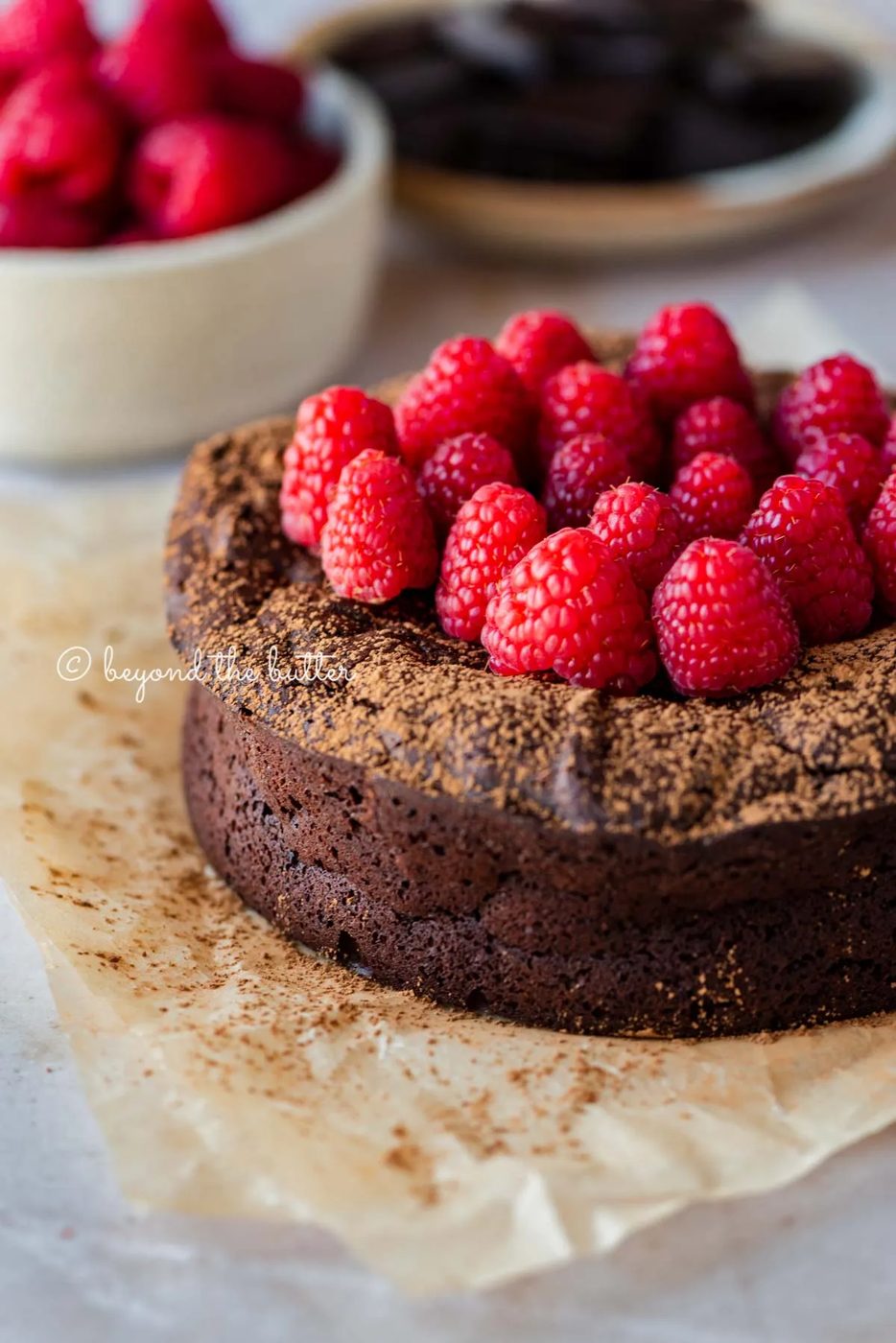 Small flourless chocolate cake topped with cocoa powder and fresh raspberries on parchment paper | All images © Sovuh