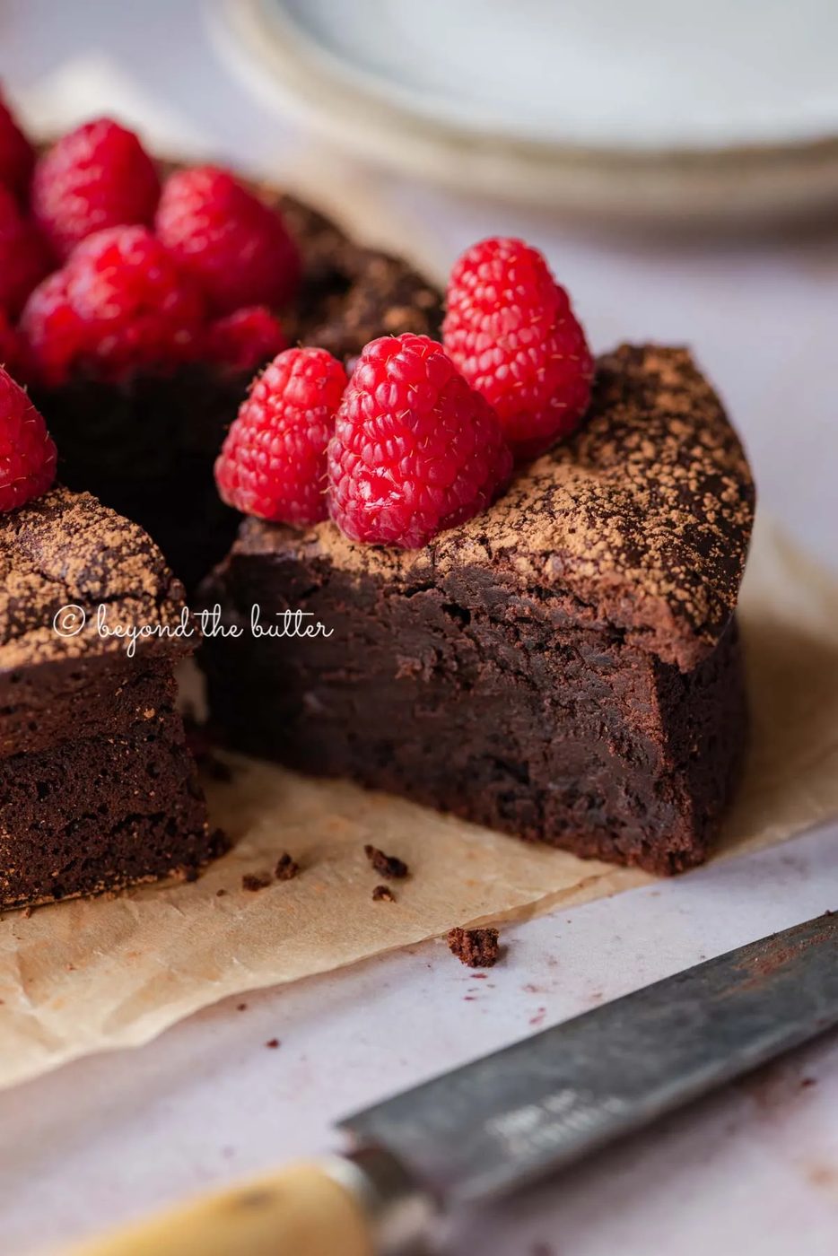 Sliced small flourless chocolate cake topped with cocoa powder and fresh raspberries on parchment paper | All images © Sovuh
