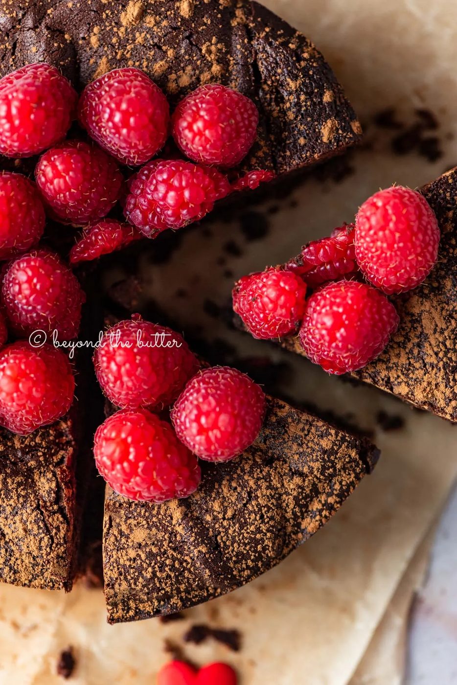 Sliced small flourless chocolate cake topped with cocoa powder and fresh raspberries on parchment paper | All images © Sovuh