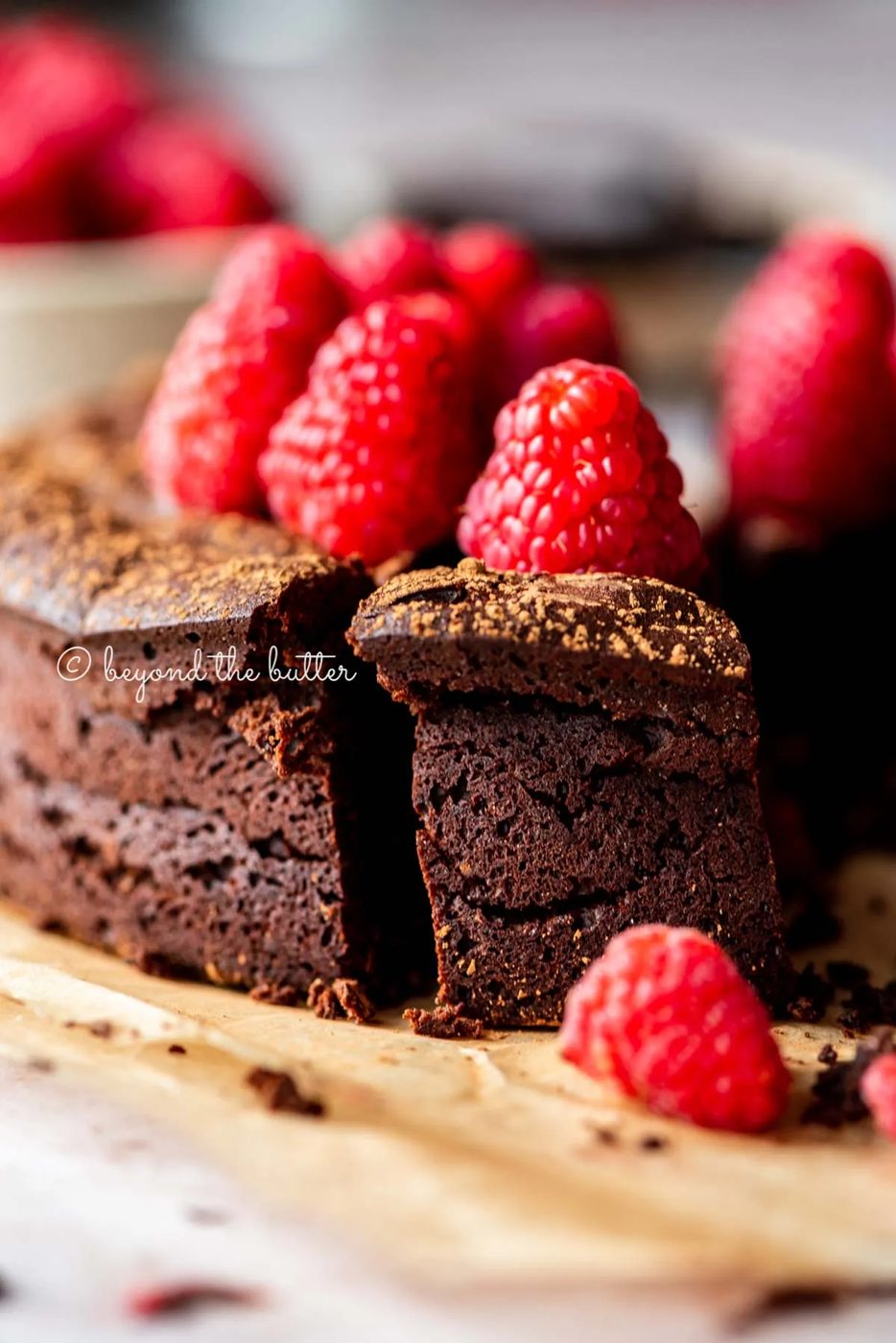 Sliced small flourless chocolate cake topped with cocoa powder and fresh raspberries on parchment paper | All images © Sovuh