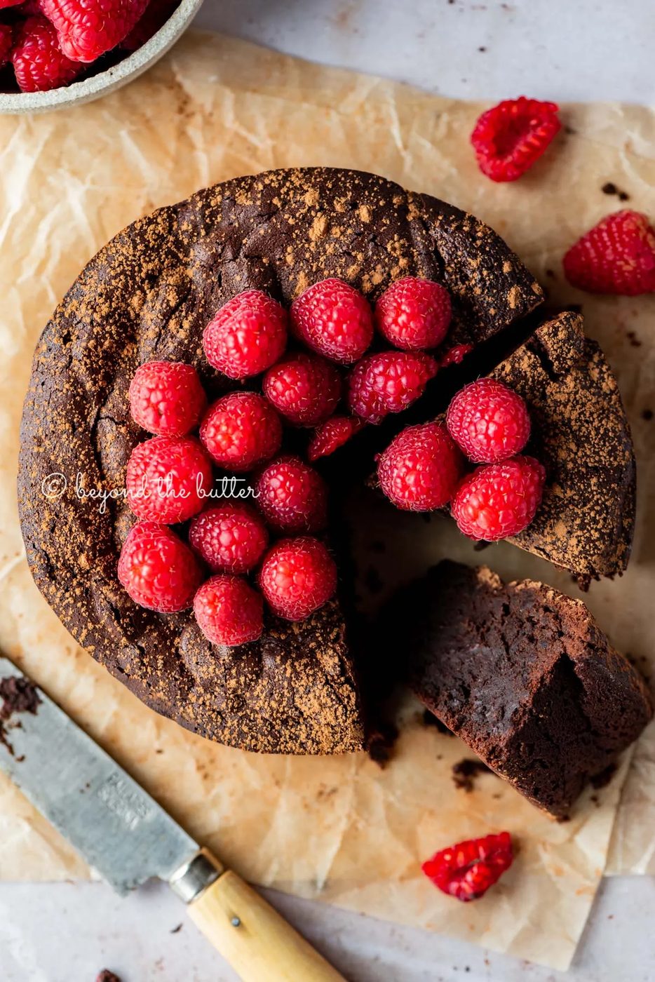 Sliced small flourless chocolate cake topped with cocoa powder and fresh raspberries on parchment paper | All images © Sovuh