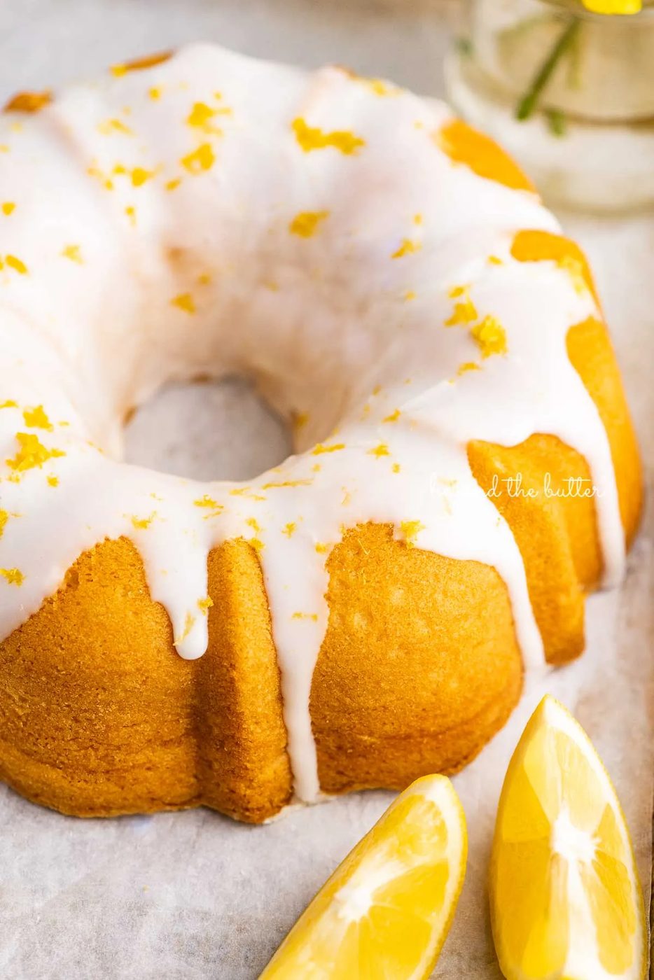 Small lemon cream cheese pound cake topped with a simple lemon glaze on a parchment paper lined baking sheet with sliced lemons | © Sovuh