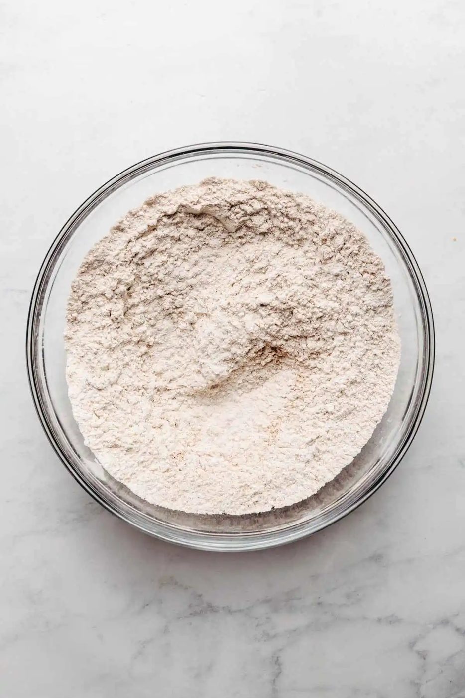 Whisked all purpose flour, ground cloves, ground ginger, ground cinnamon, and salt in a glass mixing bowl on a white and grey marbled background.